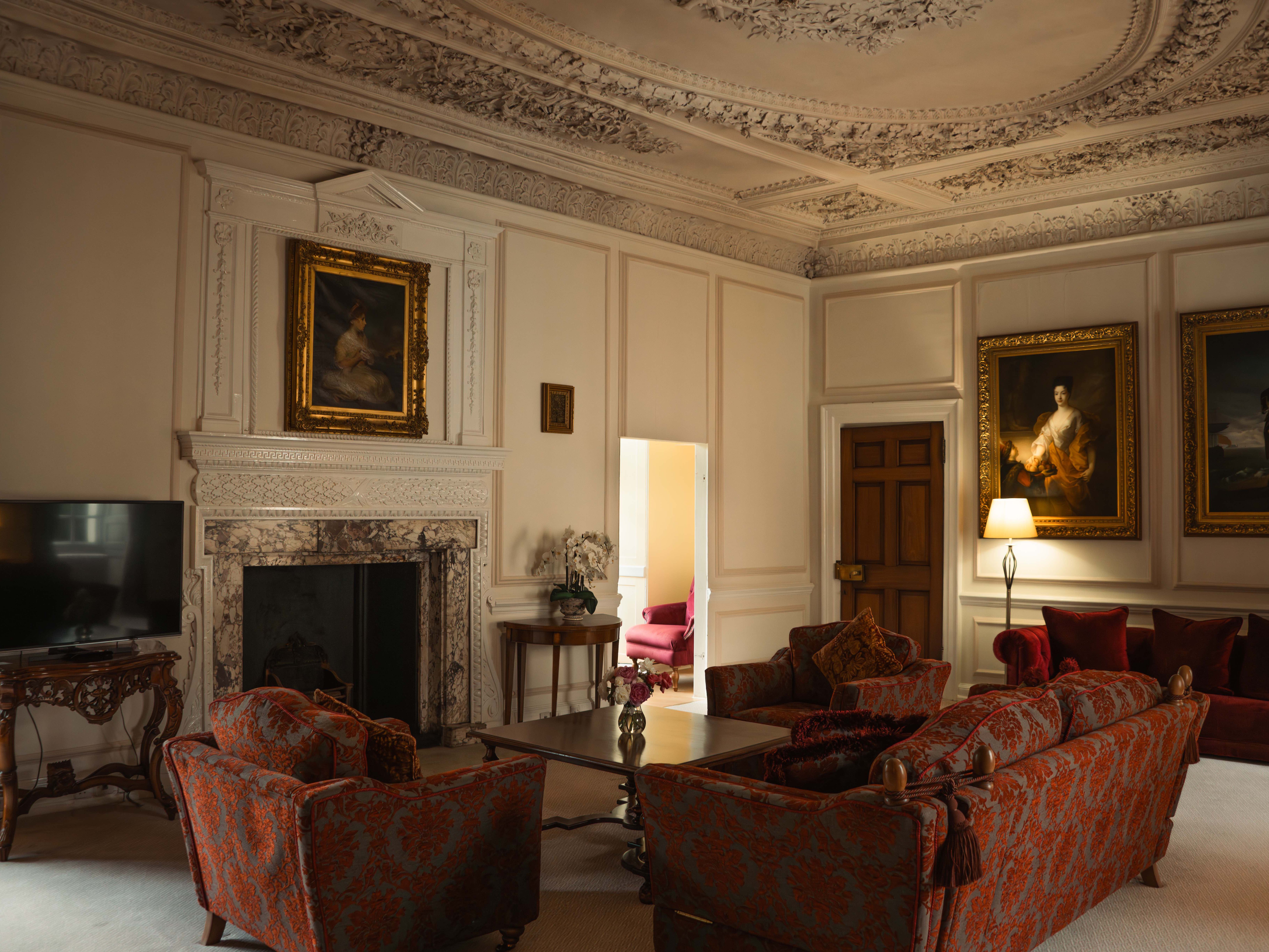 Elegant, ornately decorated living room with vintage furniture, a fireplace, and classical paintings on the walls.