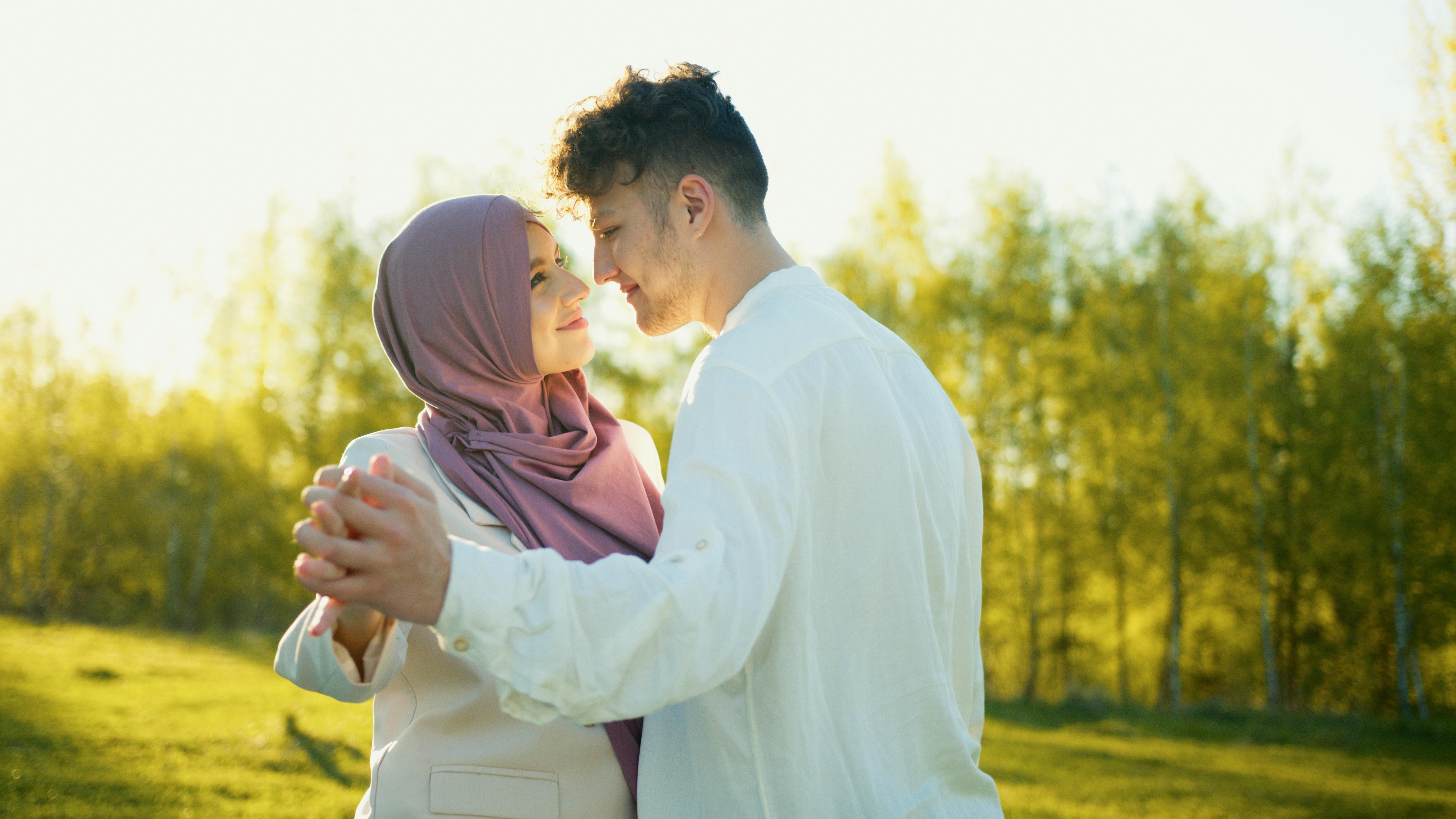 Young couple dancing outdoors, woman wearing a hijab and man in a white shirt, smiling at each other