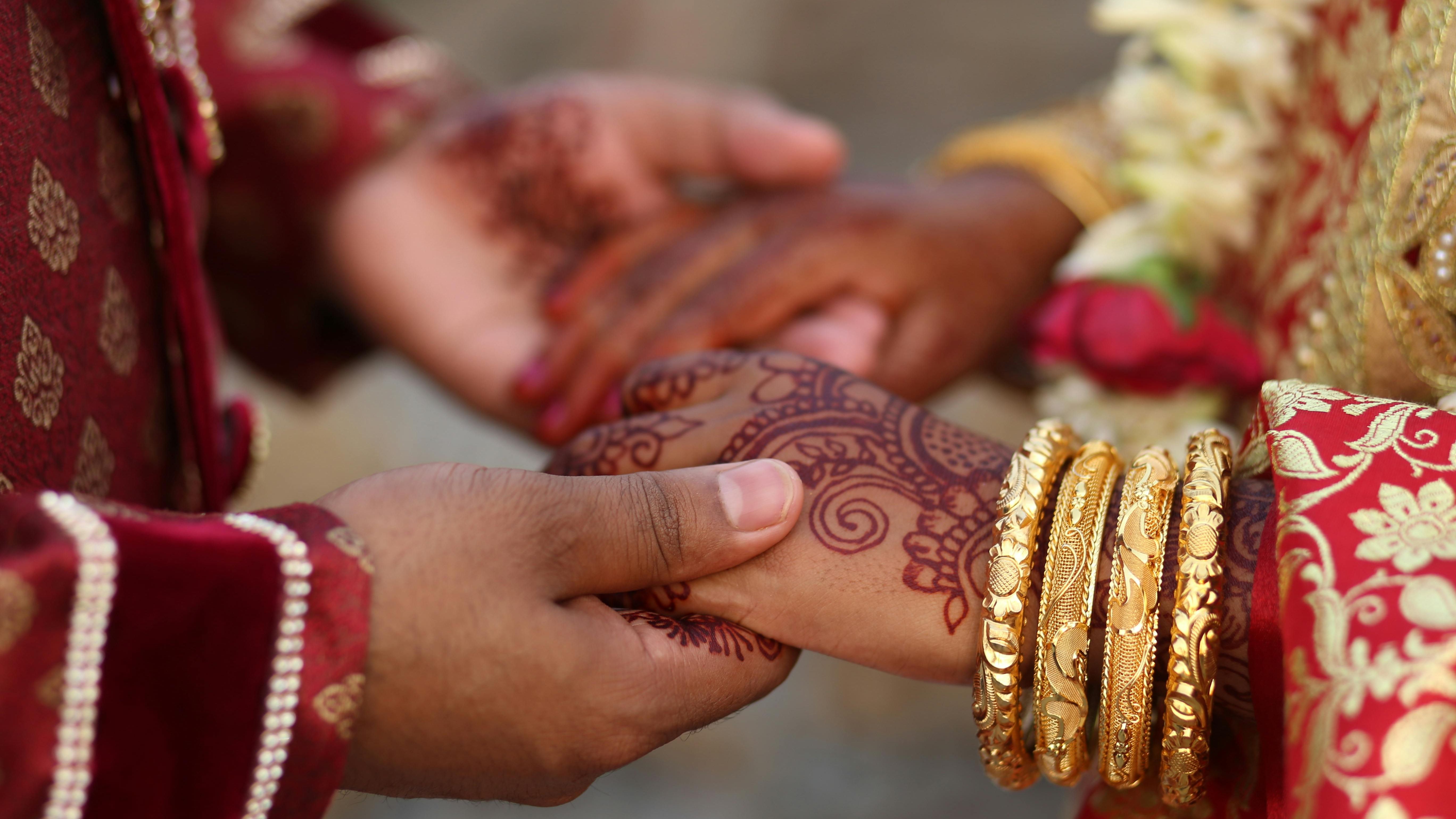 Close-up of a couple holding hands during a traditional Pakistani wedding ceremony, with intricate henna designs and gold bangles.