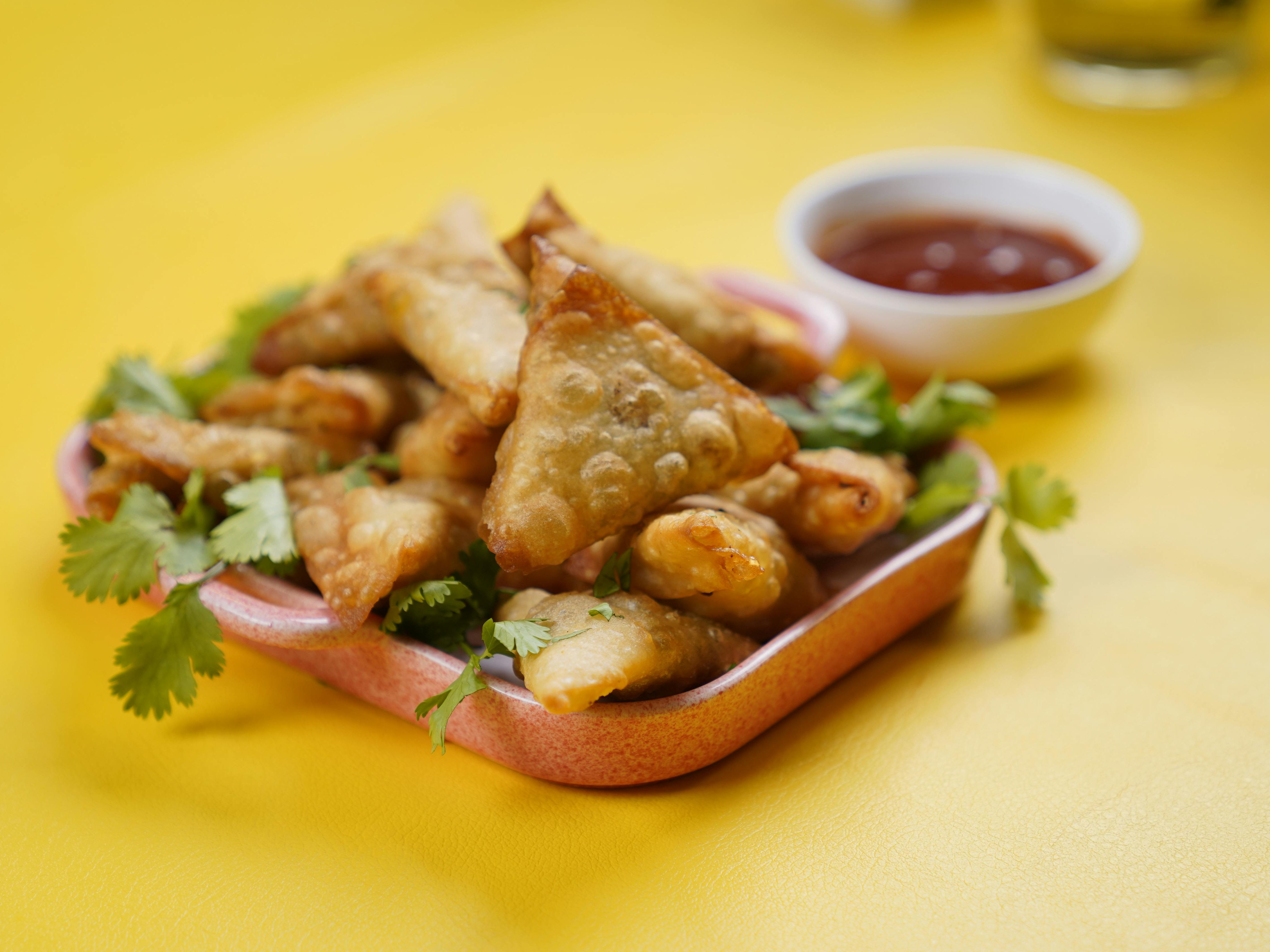 Plate of crispy samosas with coriander and dipping sauce