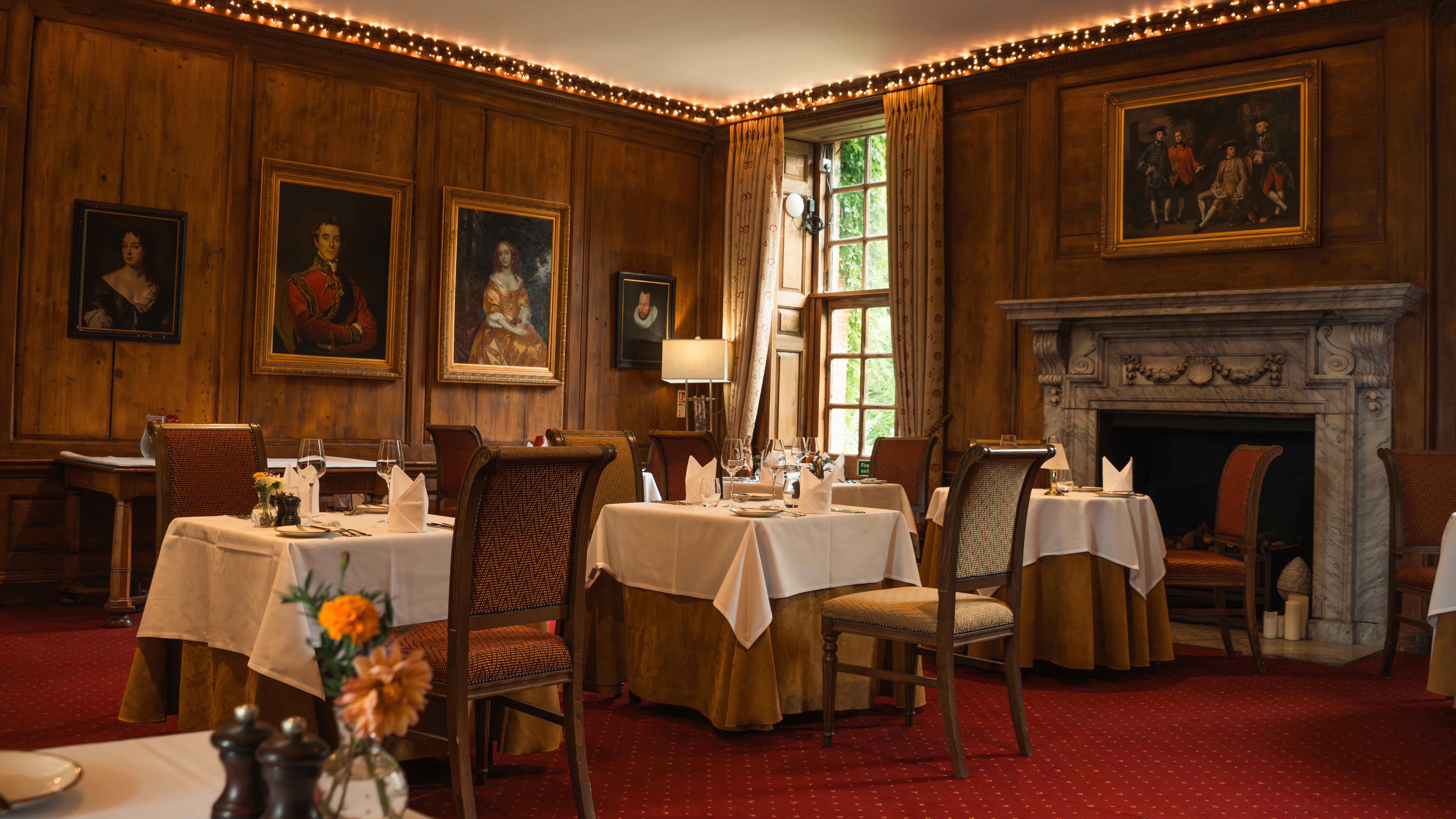 Elegant restaurant dining room with classic portraits, wooden paneling, and fireplace