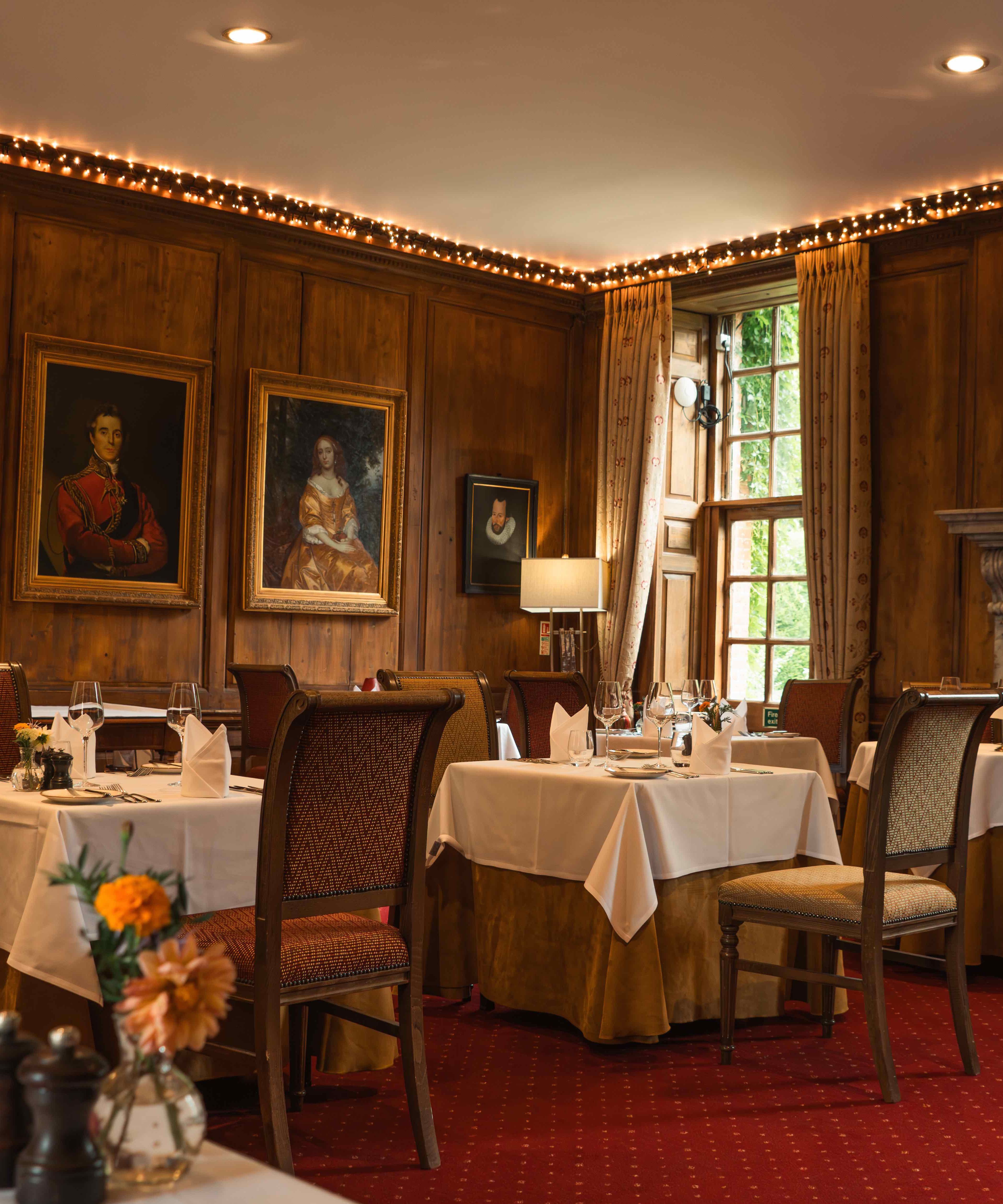 Elegant restaurant dining room with classic portraits, wooden paneling, and fireplace