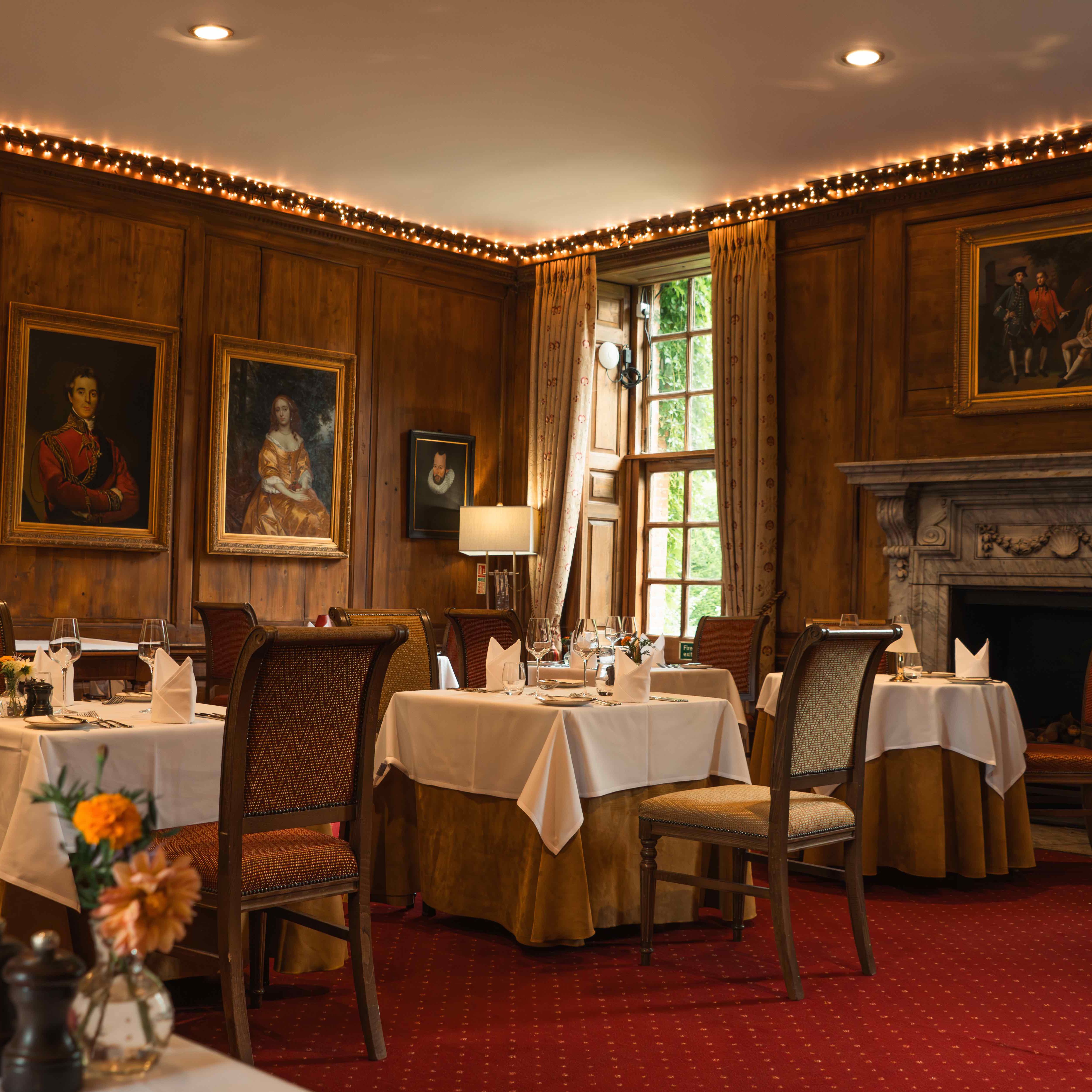 Elegant restaurant dining room with classic portraits, wooden paneling, and fireplace