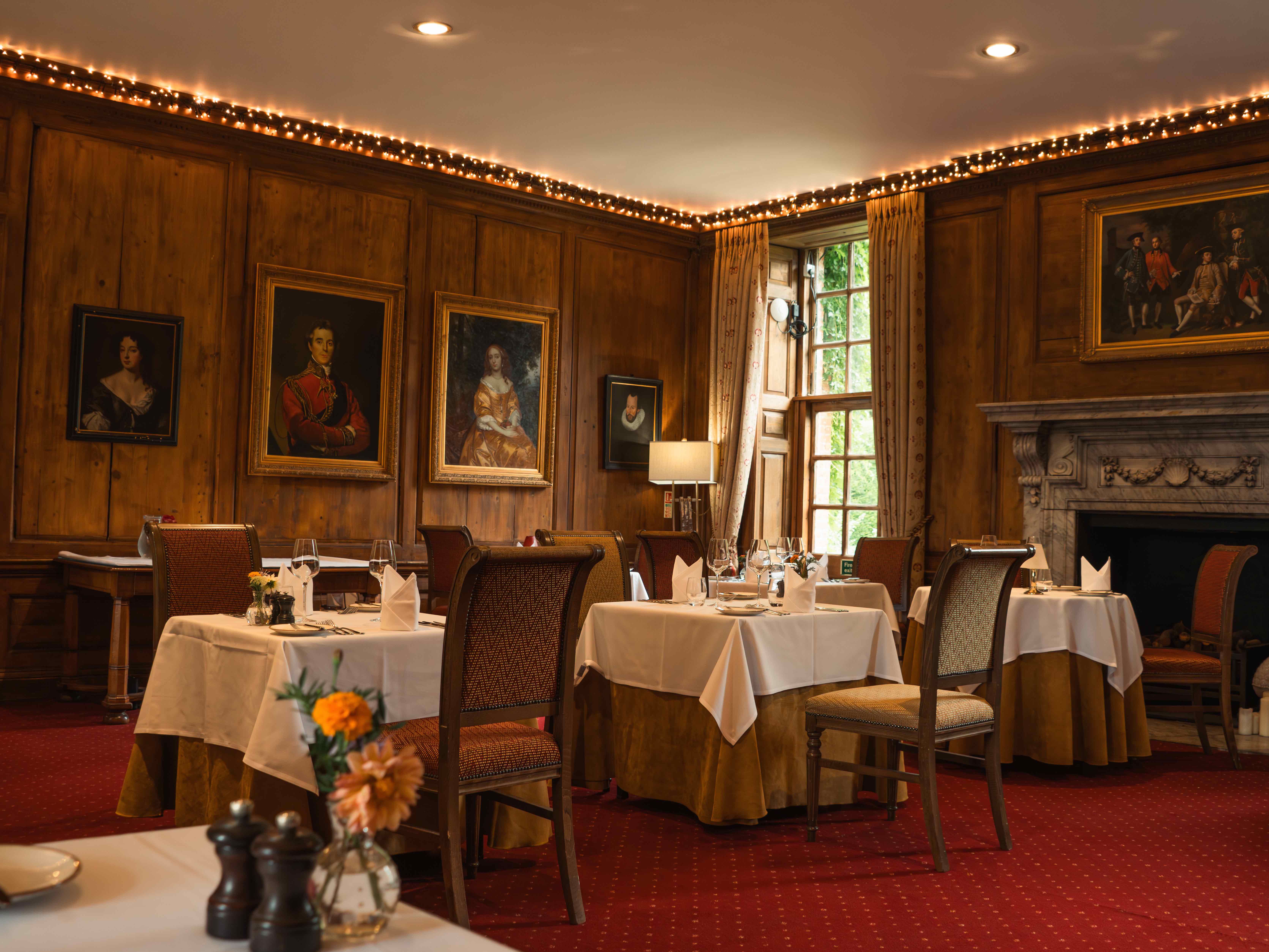 Elegant restaurant dining room with classic portraits, wooden paneling, and fireplace