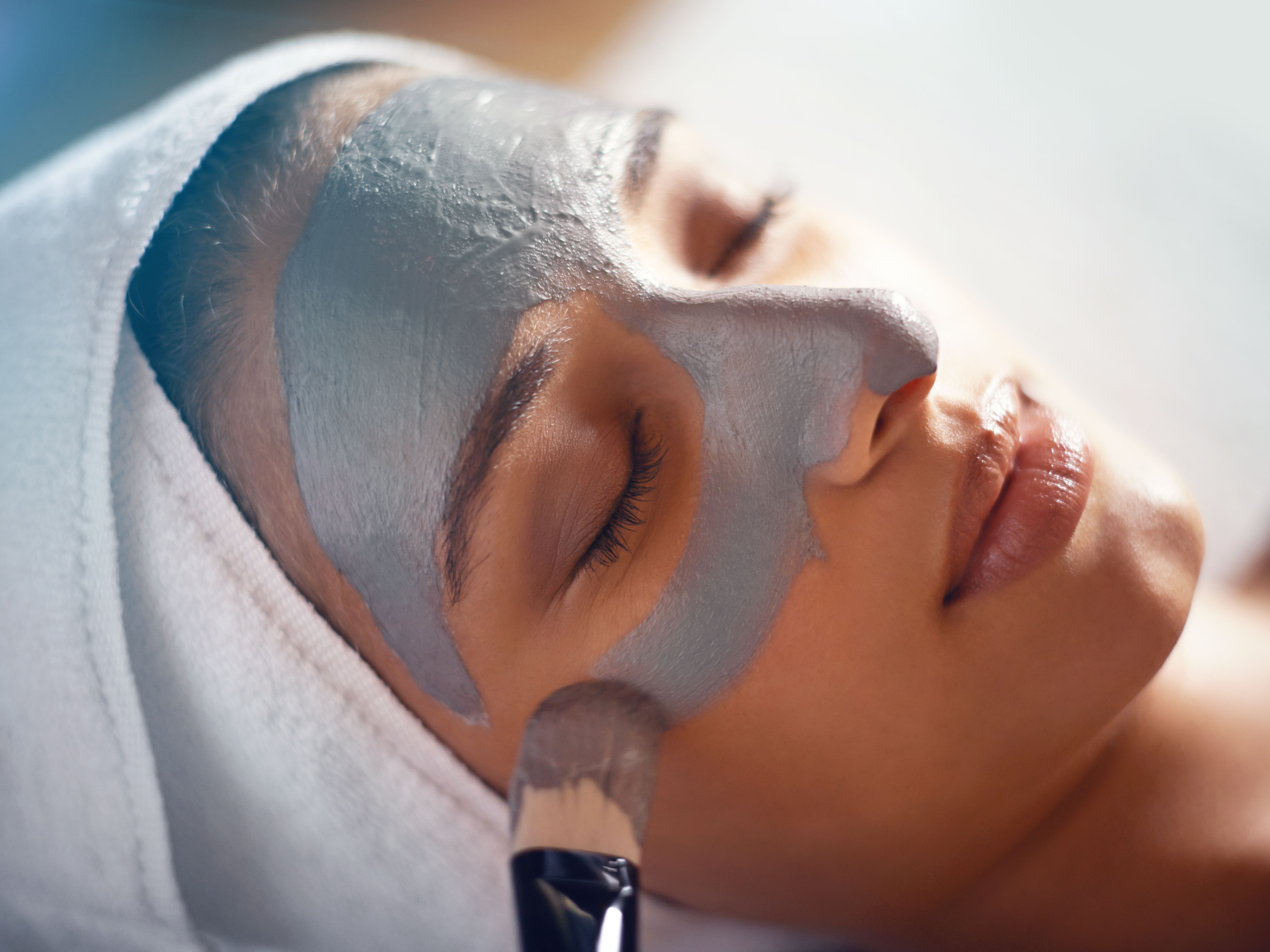 Woman relaxing while getting a facial mask applied at a spa