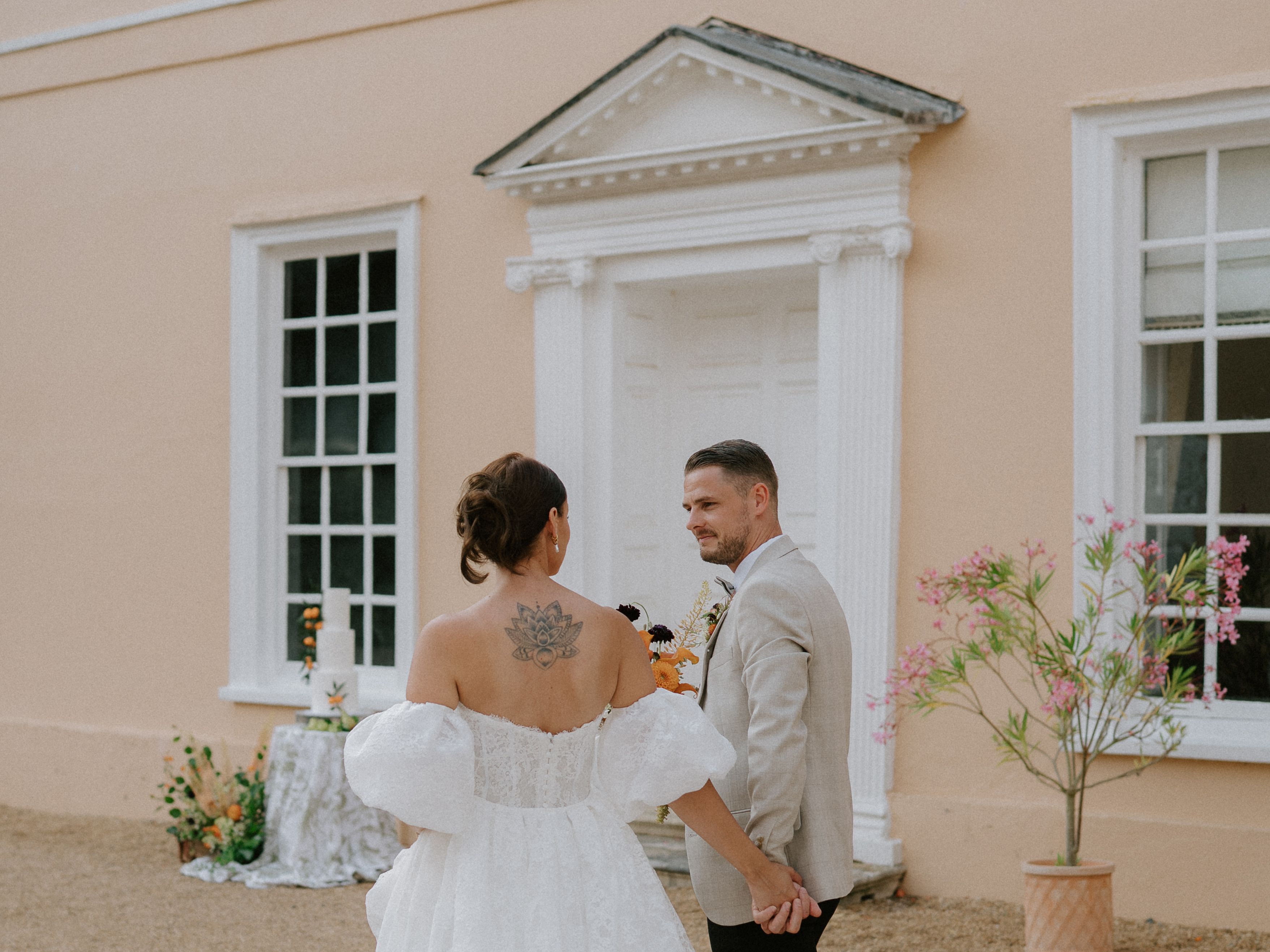 Bride in a white wedding dress holding hands with a groom in a light suit outside a classical building.