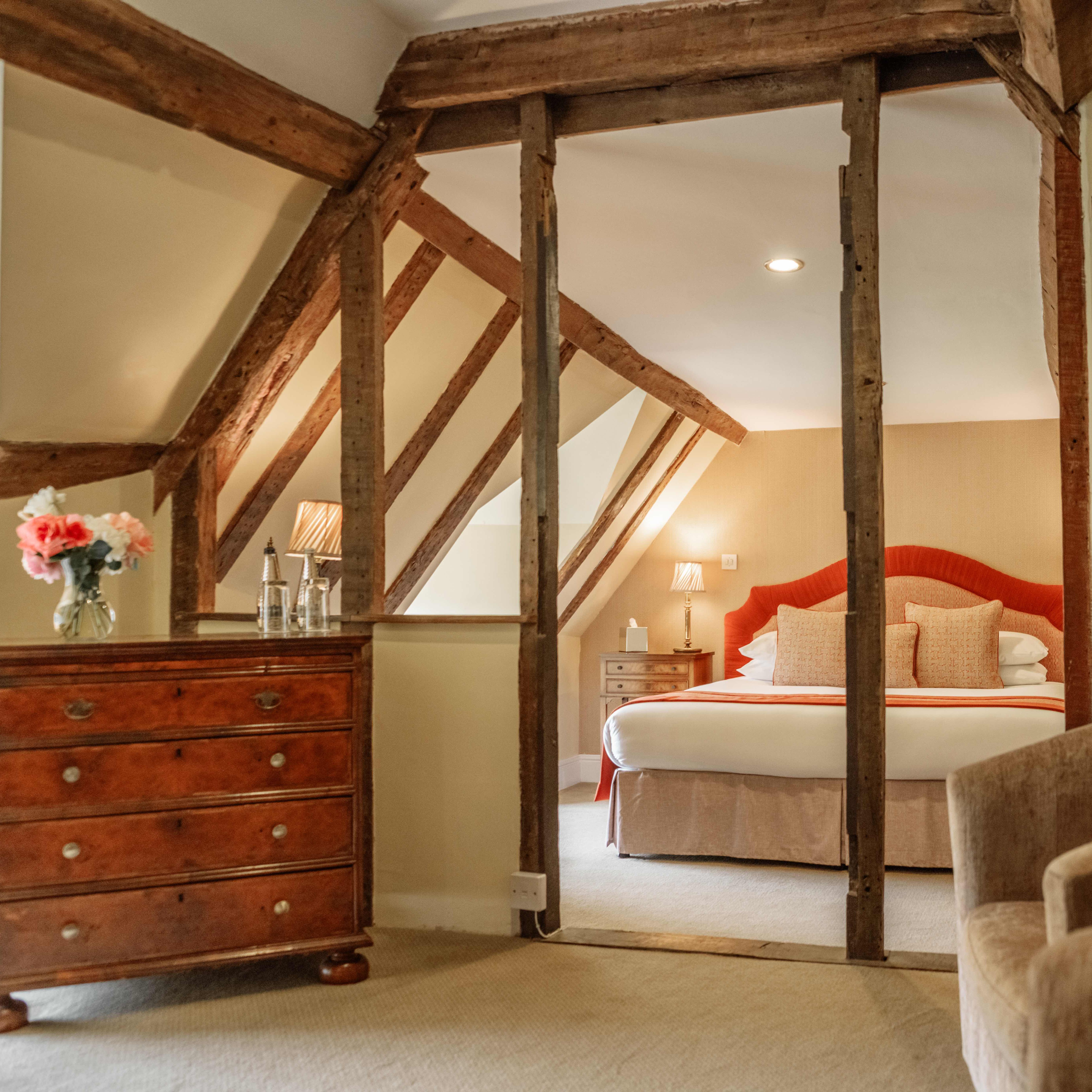 Cozy attic bedroom with wooden beams, a large bed, wooden chest of drawers, and armchair.