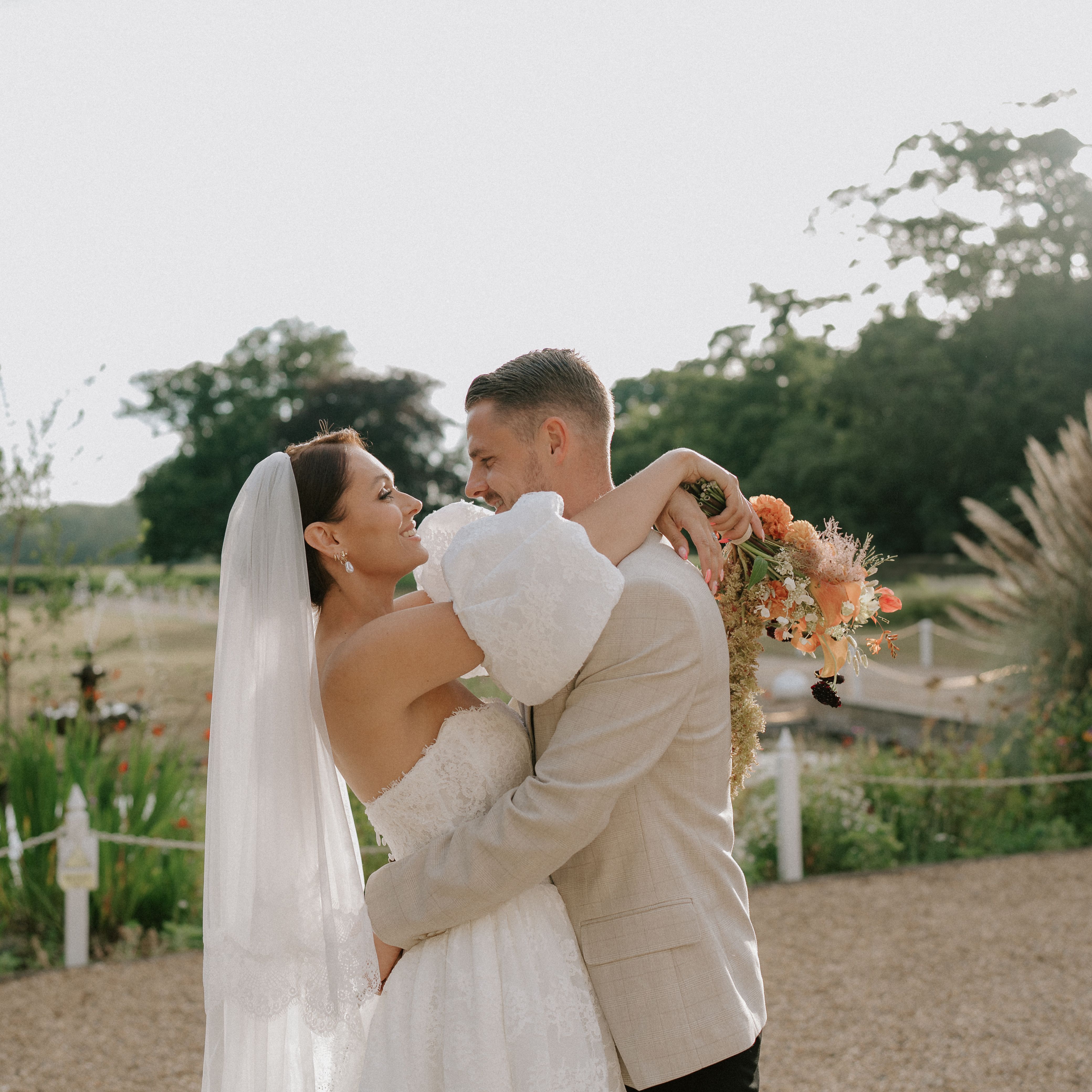 Bride and groom embracing outdoors on their wedding day, with the bride holding a bouquet of flowers.