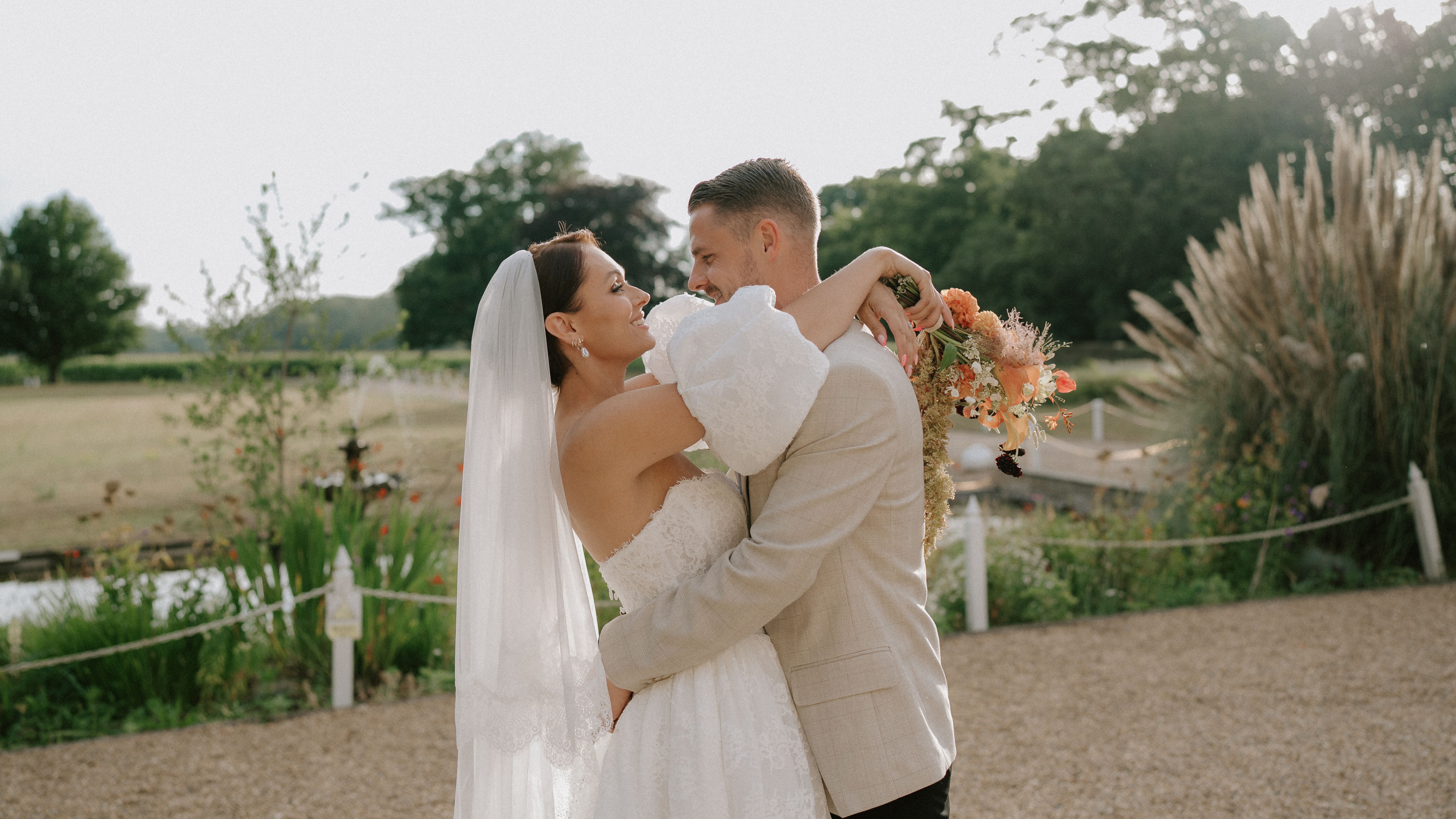 Bride and groom embracing outdoors on their wedding day, with the bride holding a bouquet of flowers.