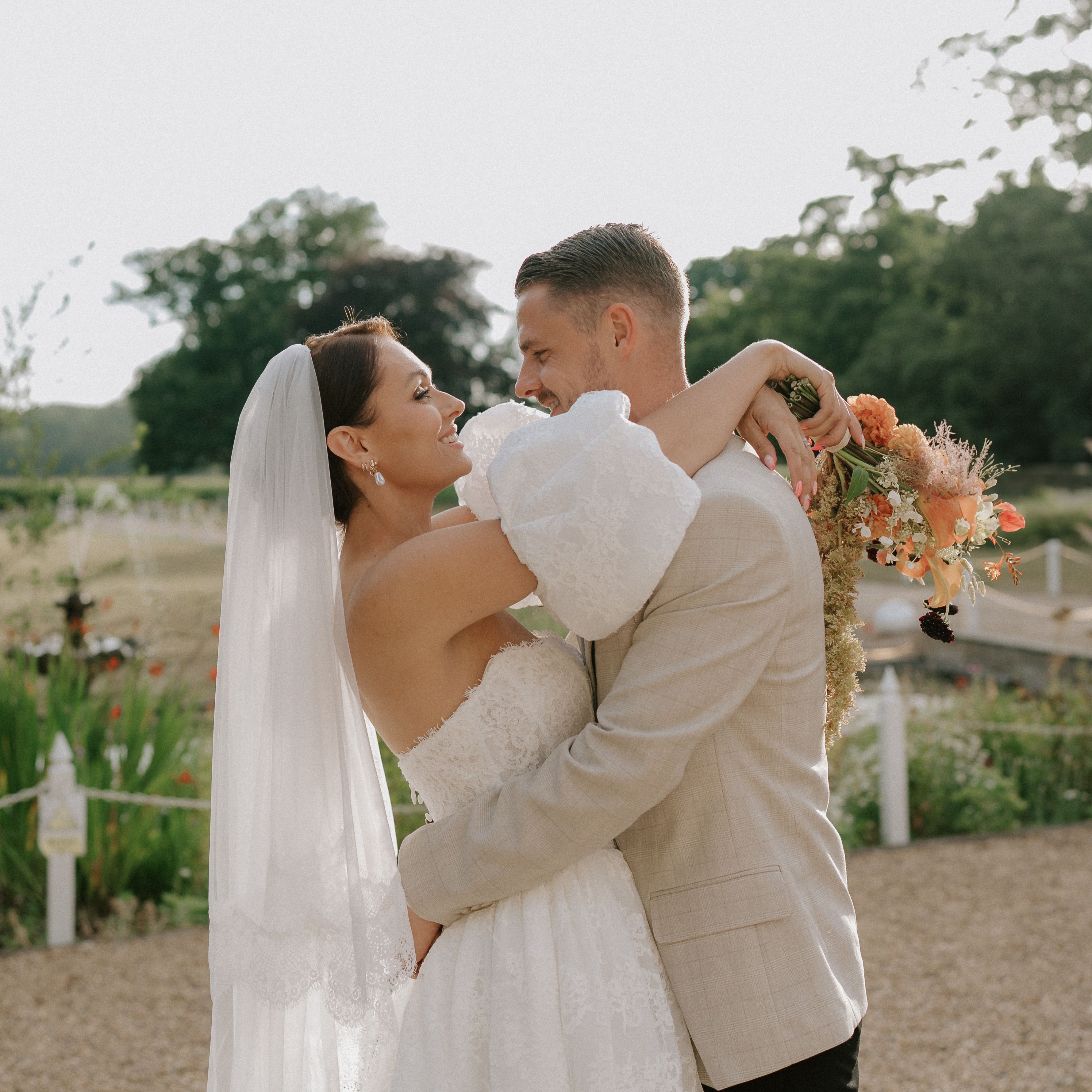 Bride and groom embracing outdoors on their wedding day, with the bride holding a bouquet of flowers.