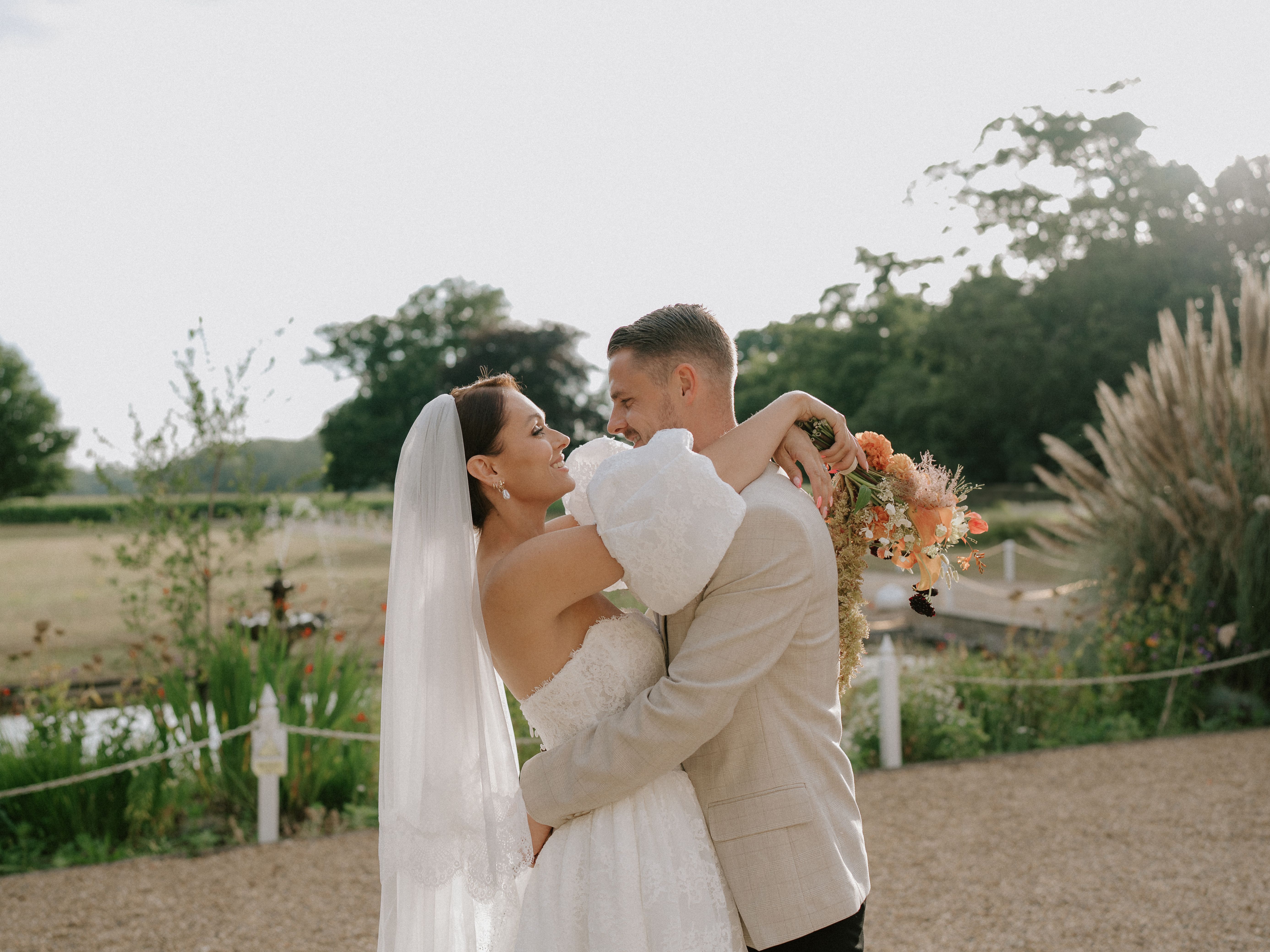 Bride and groom embracing outdoors on their wedding day, with the bride holding a bouquet of flowers.