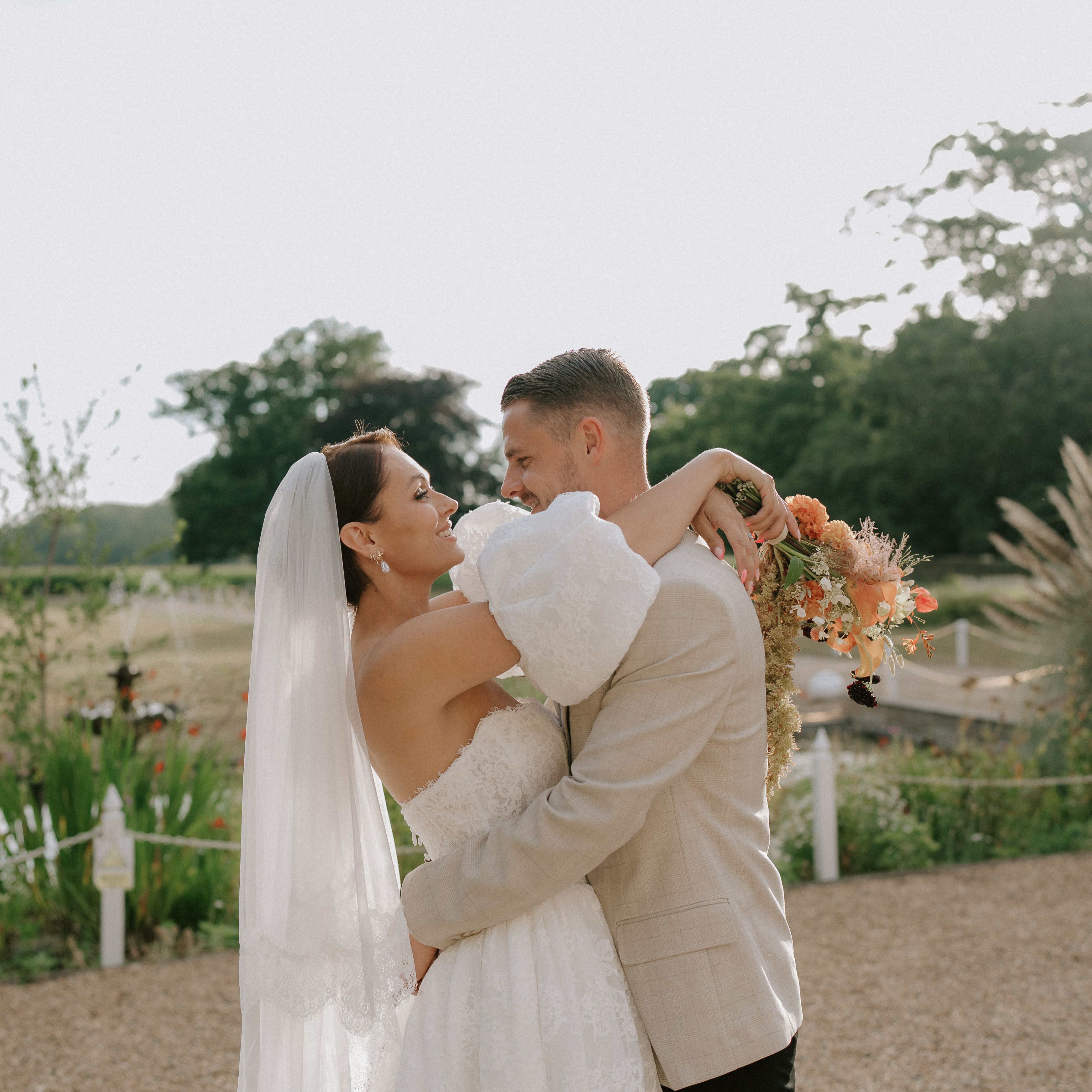 Bride and groom embracing outdoors on their wedding day, with the bride holding a bouquet of flowers.