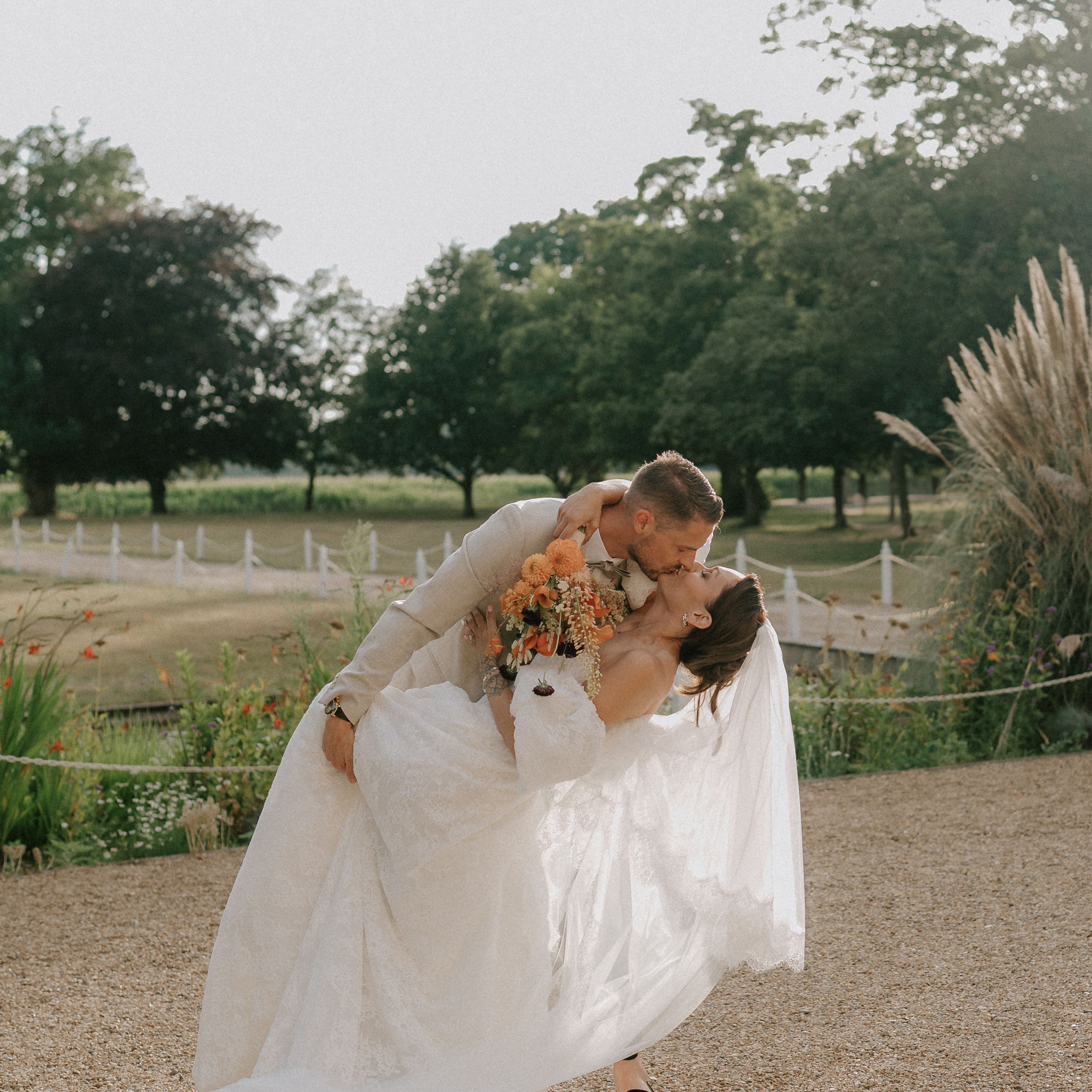 Groom dipping and kissing bride in an outdoor garden setting during their wedding.