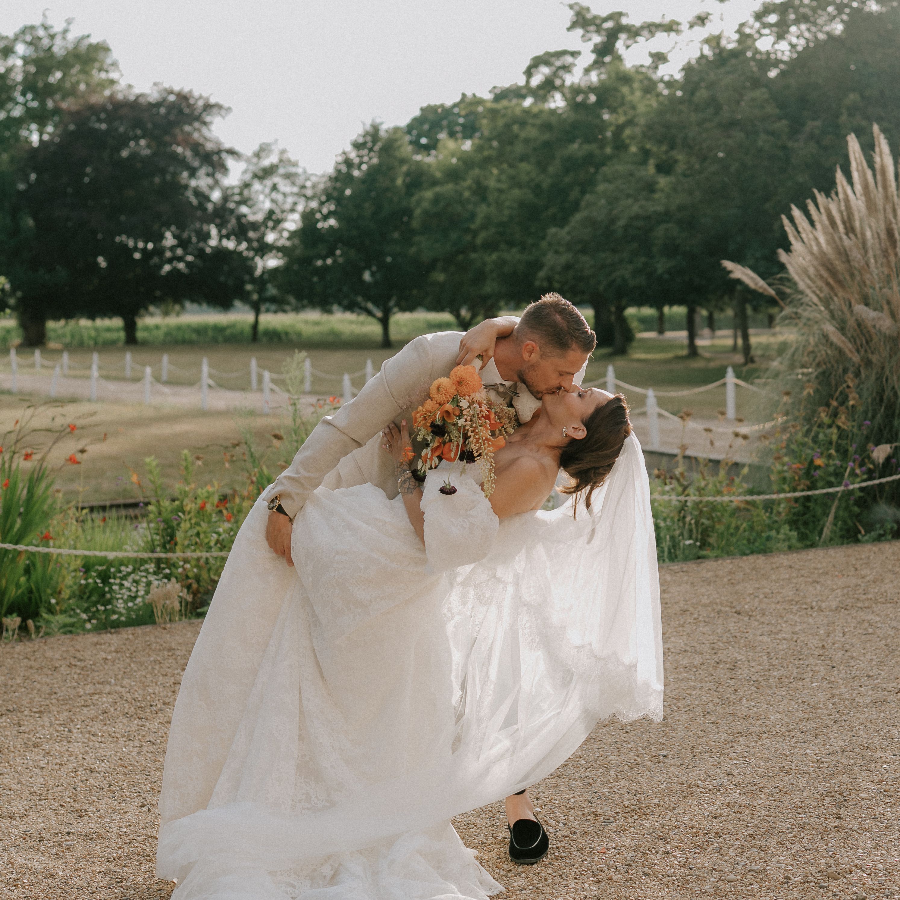 Groom dipping and kissing bride in an outdoor garden setting during their wedding.