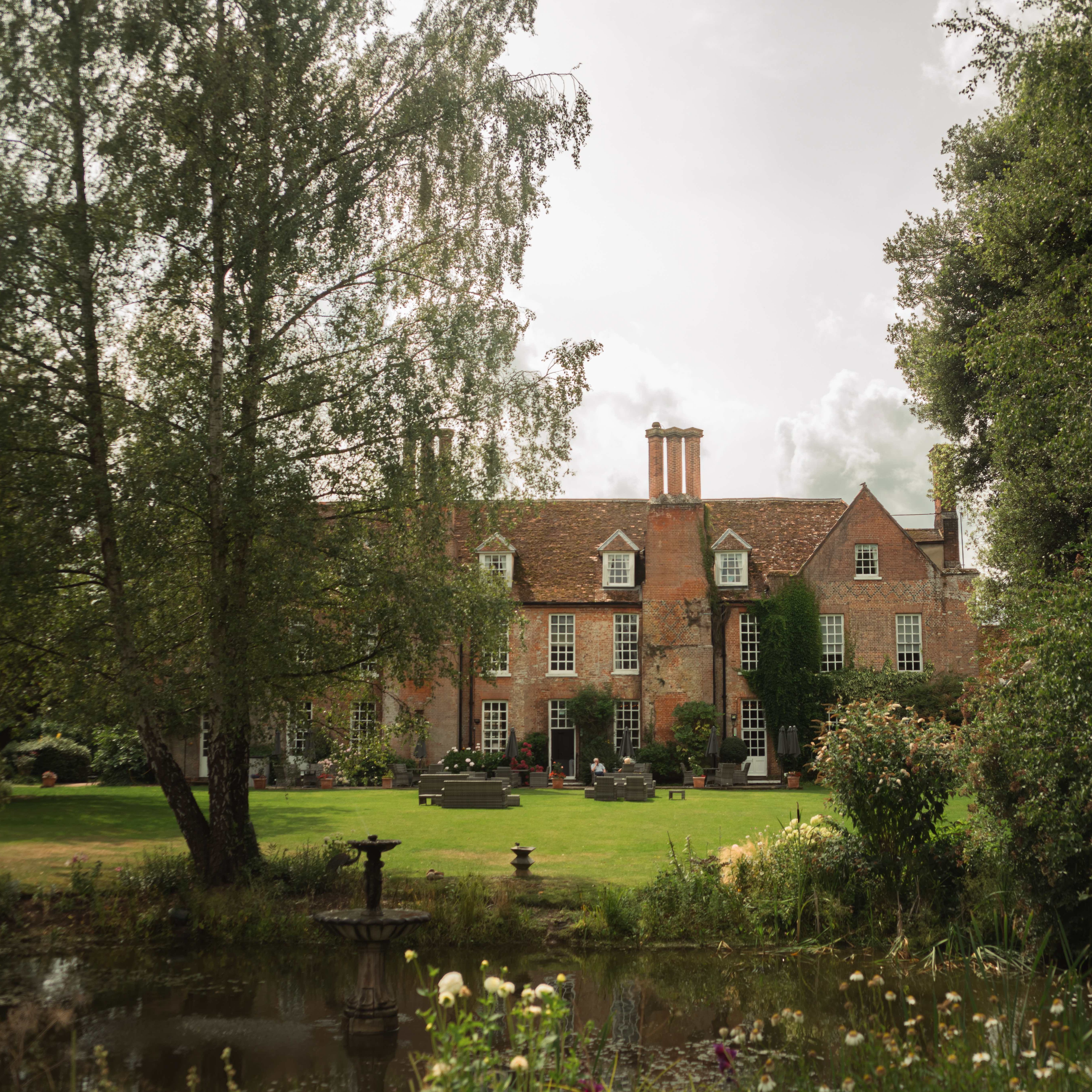 Large brick country house with a garden and pond in front, surrounded by trees