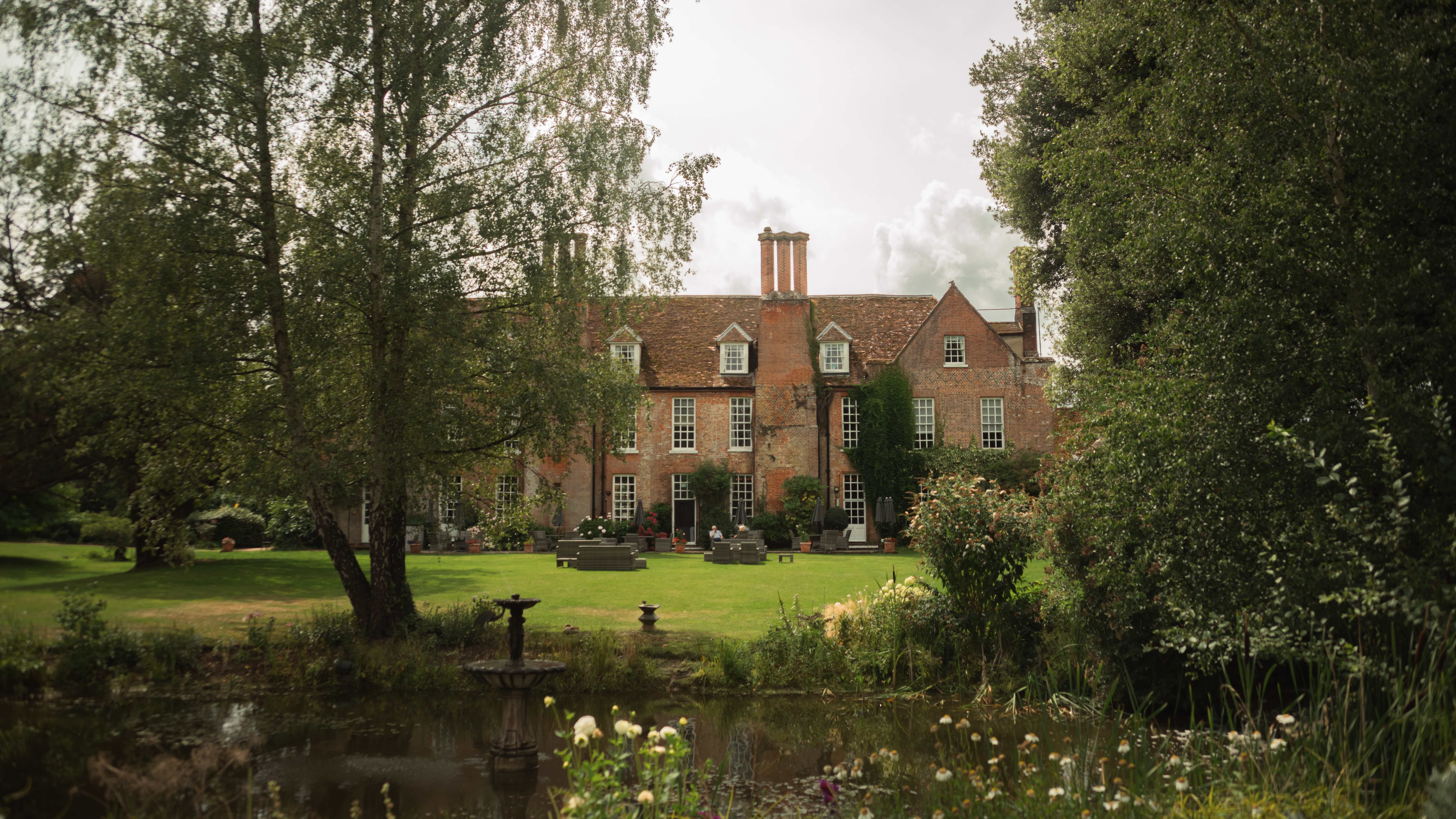 Large brick country house with a garden and pond in front, surrounded by trees