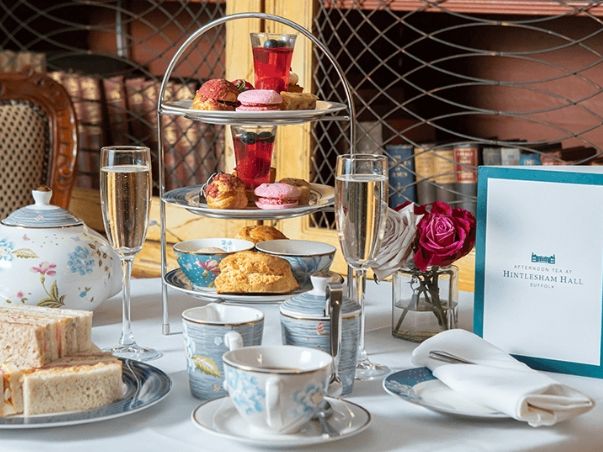 Elegant afternoon tea setup with a three-tiered tray of pastries, sandwiches, teacups, teapot, champagne glasses, and a menu card at Hintlesham Hall.
