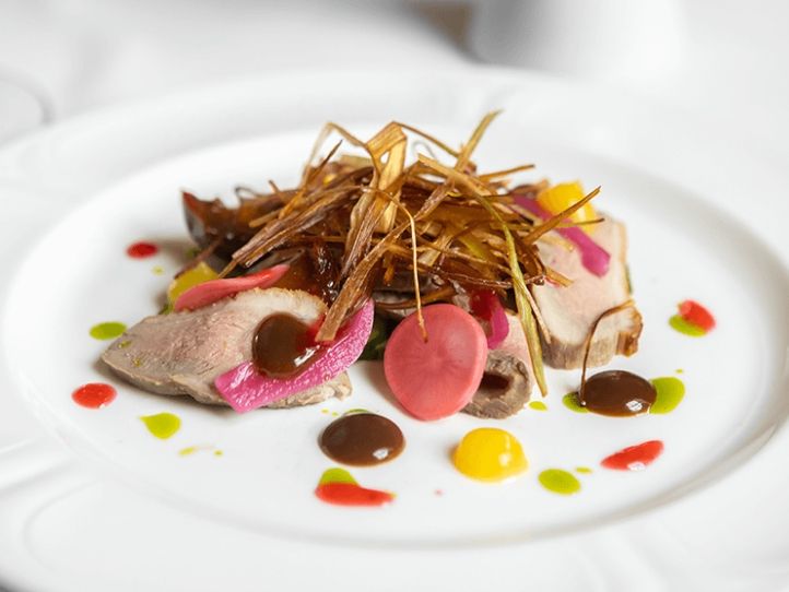 Gourmet dish with sliced meat, colorful sauces, and crispy garnish on a white plate