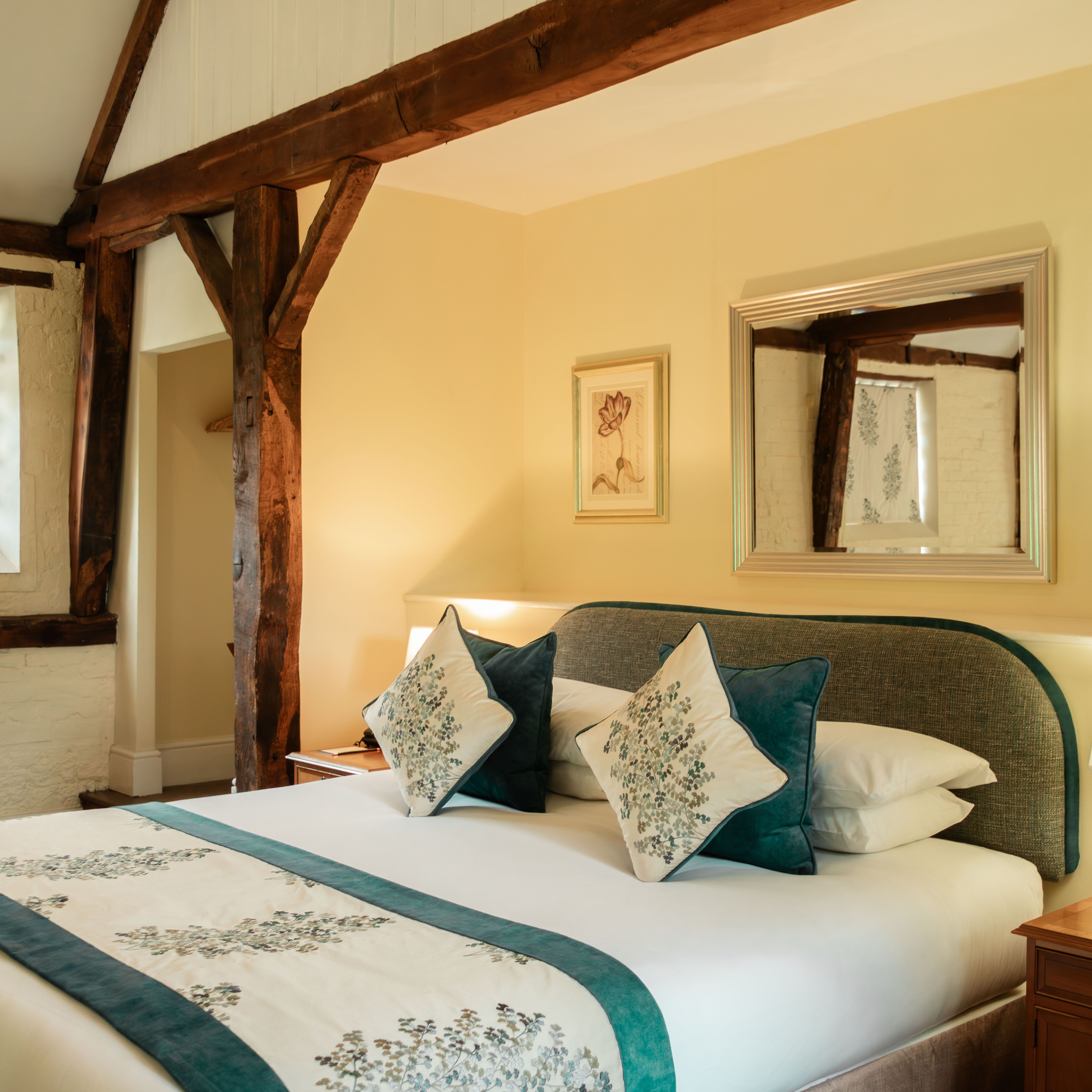 Cozy bedroom with wooden beams, a double bed with floral pillows, and a bedside lamp.