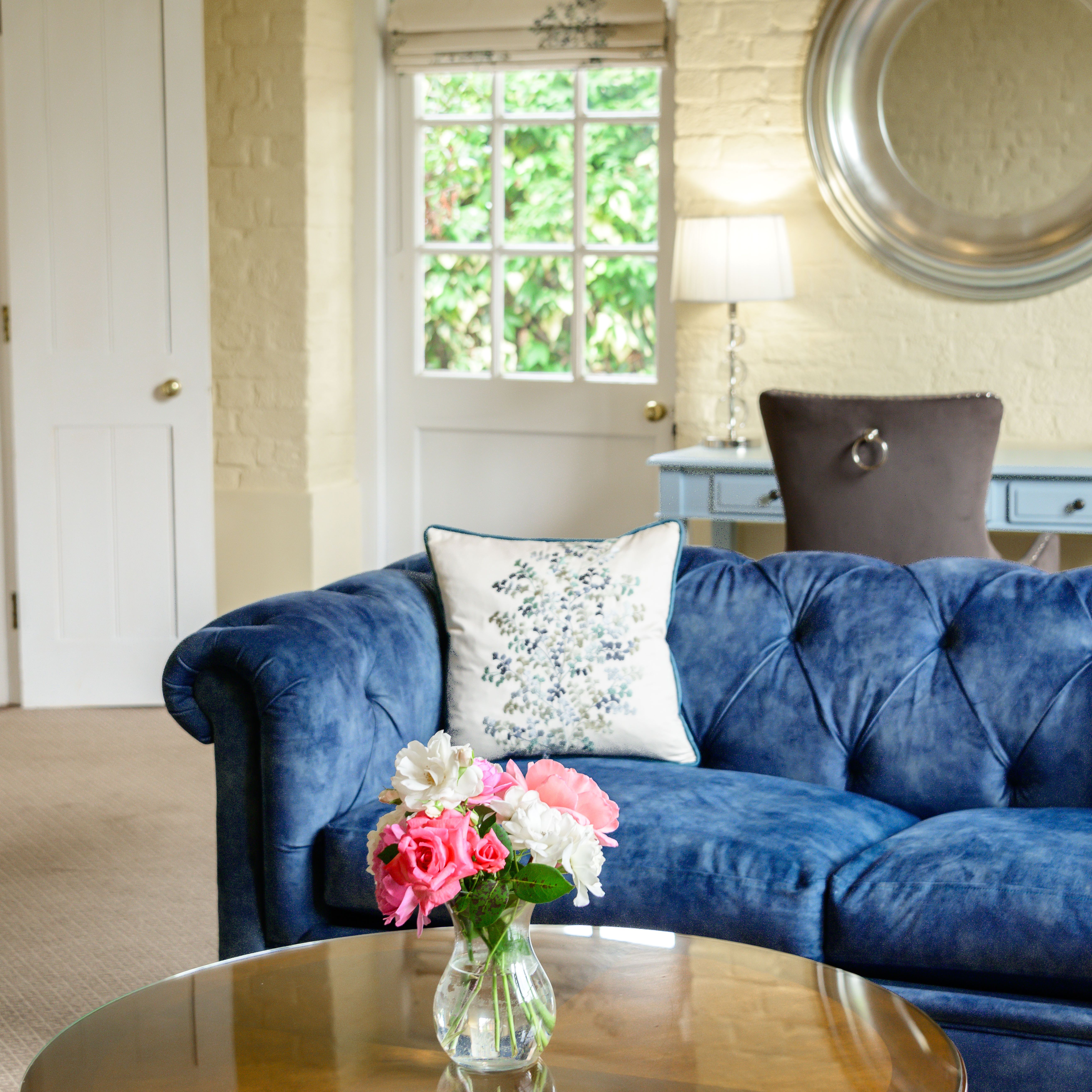 Cozy living room with blue sofa, floral pillow, and a vase of flowers on a glass coffee table
