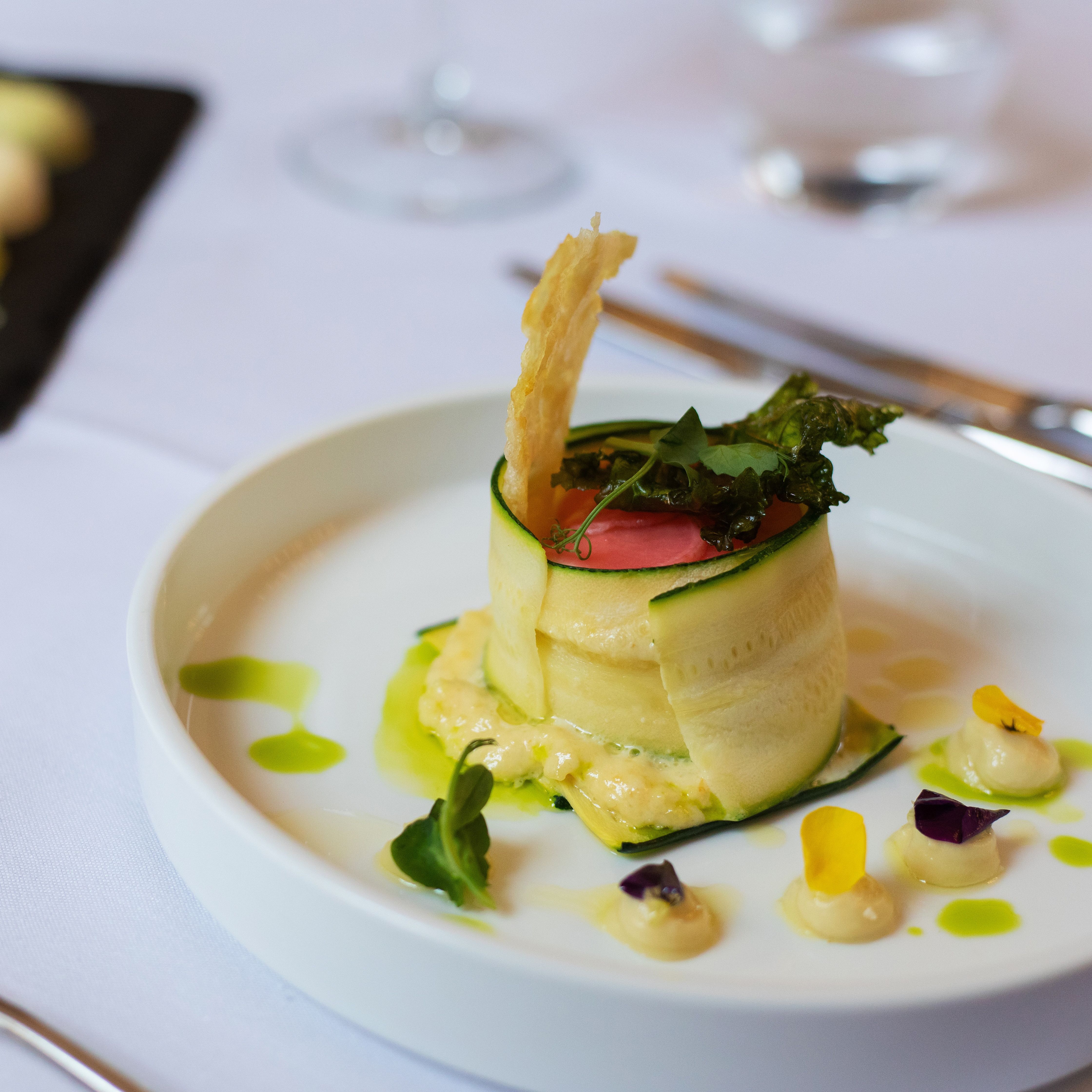 Gourmet plated dish with thinly sliced vegetables and garnishes, served on a white plate.