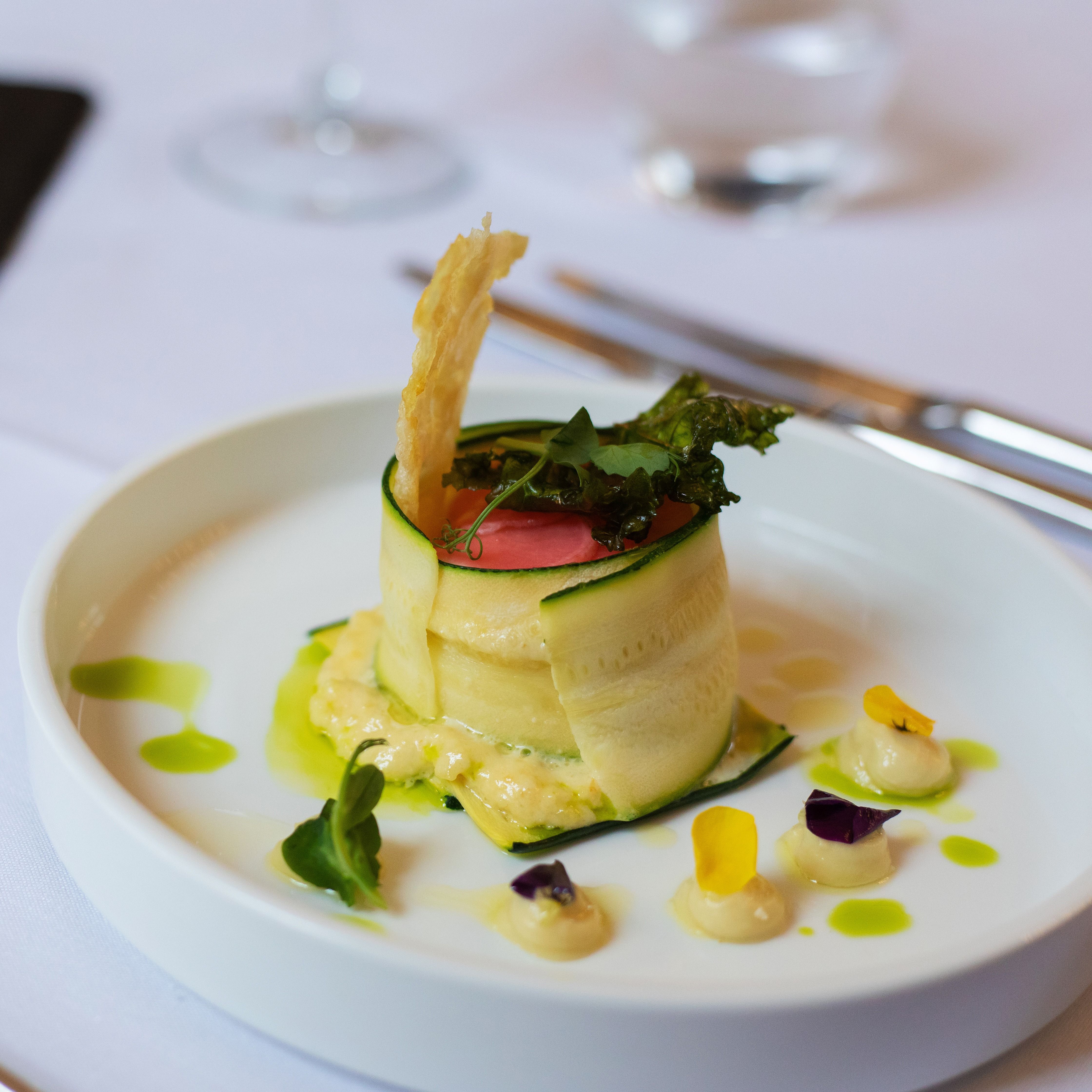 Gourmet plated dish with thinly sliced vegetables and garnishes, served on a white plate.