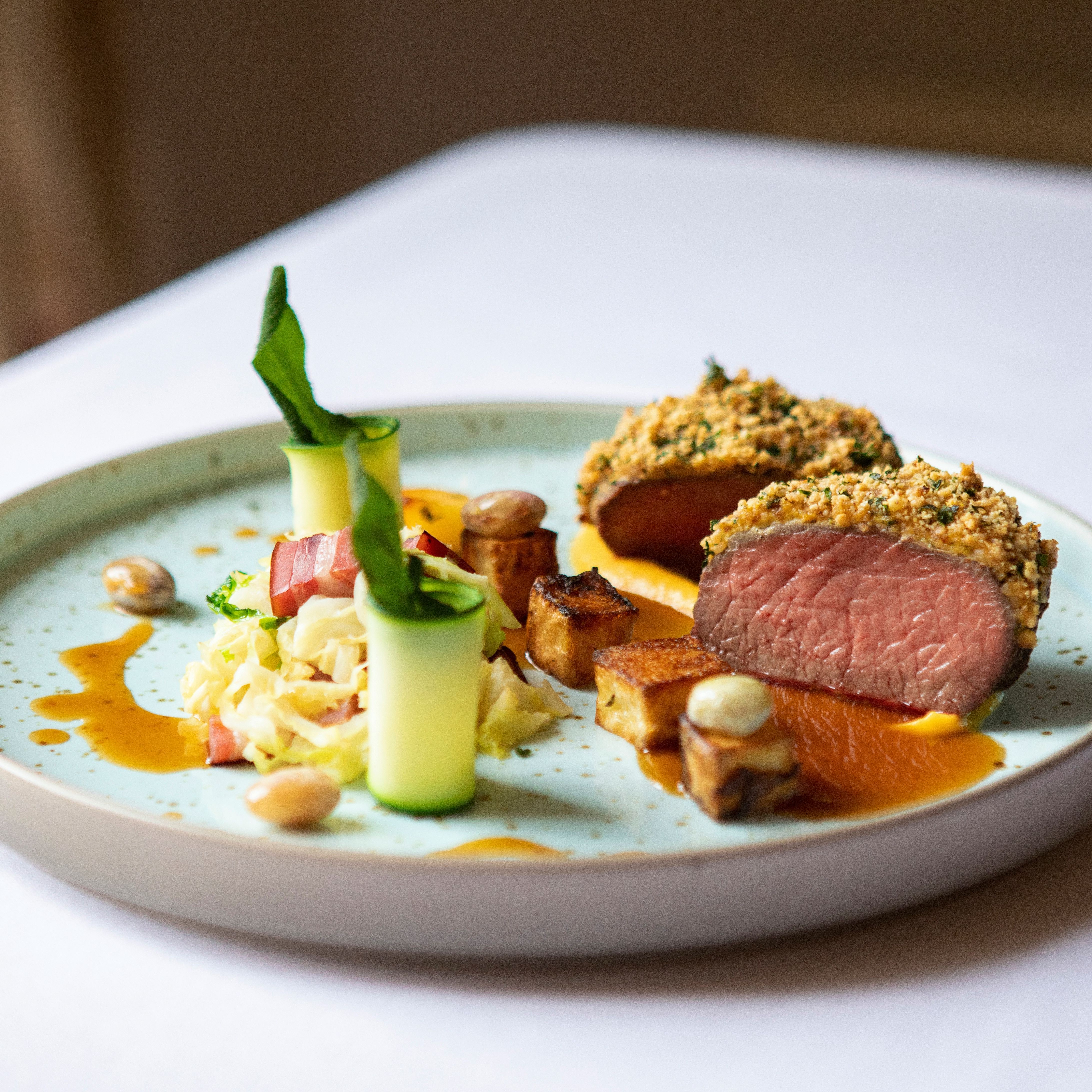 Plated gourmet dish with sliced, herb-crusted meat, vegetables, and sauce