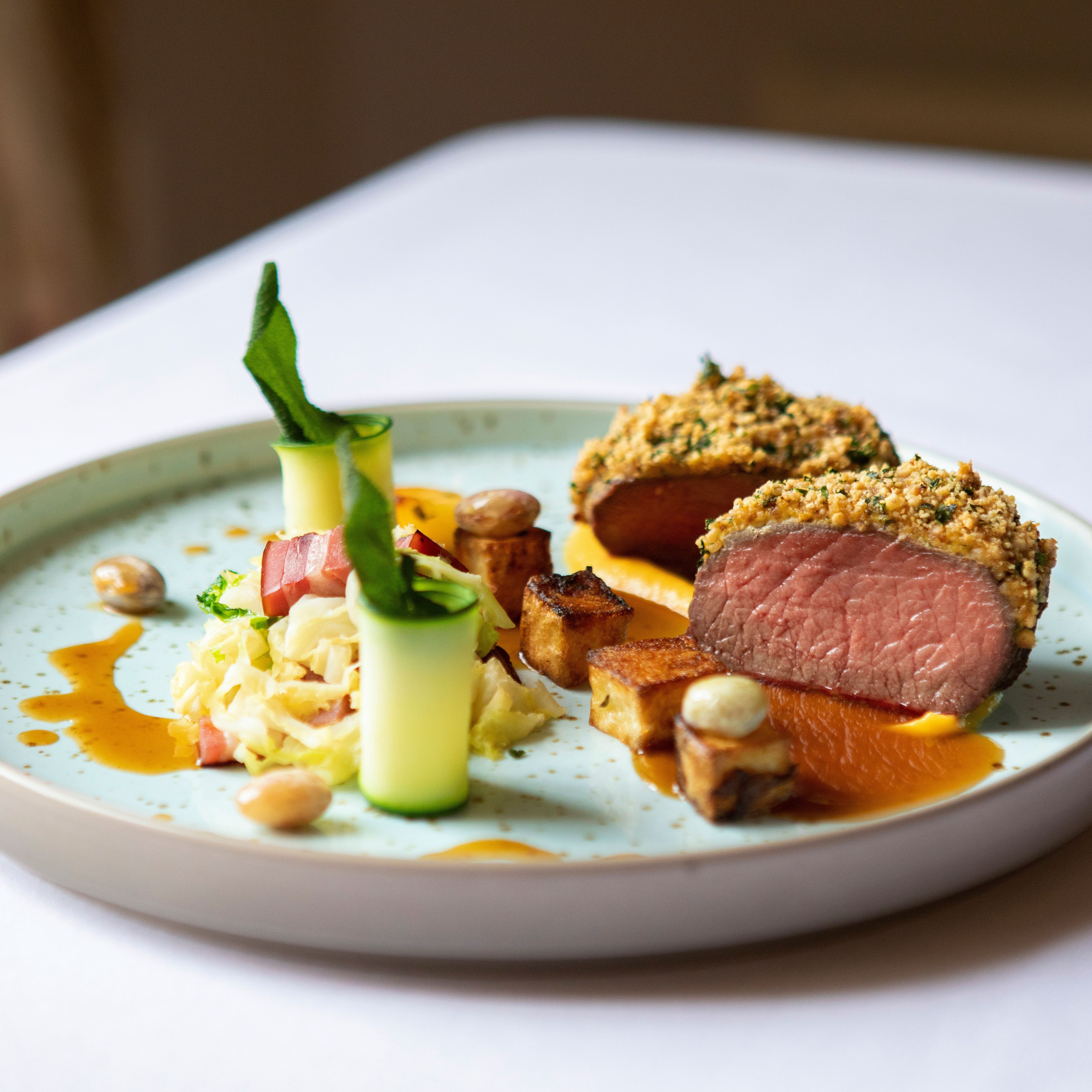 Plated gourmet dish with sliced, herb-crusted meat, vegetables, and sauce