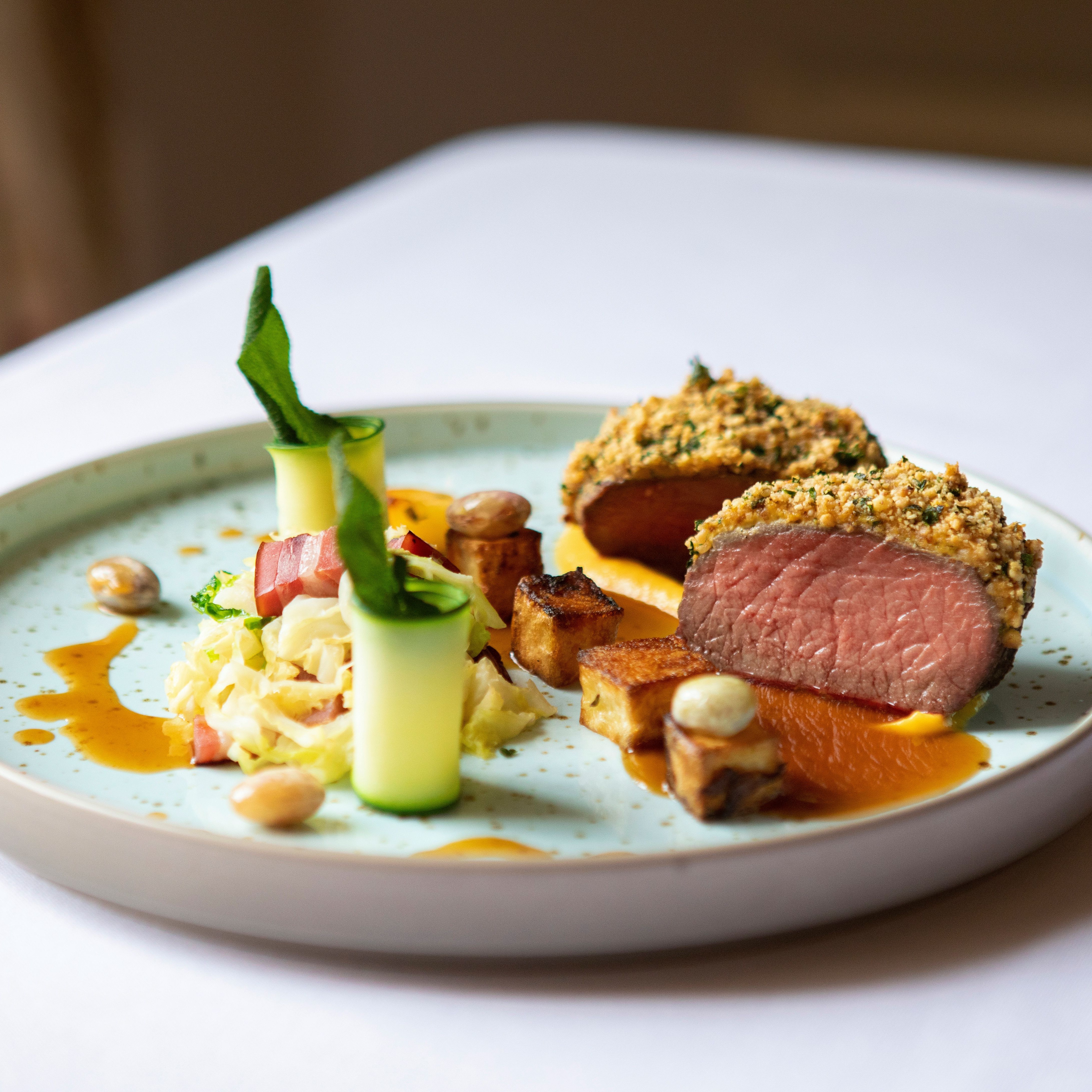 Plated gourmet dish with sliced, herb-crusted meat, vegetables, and sauce
