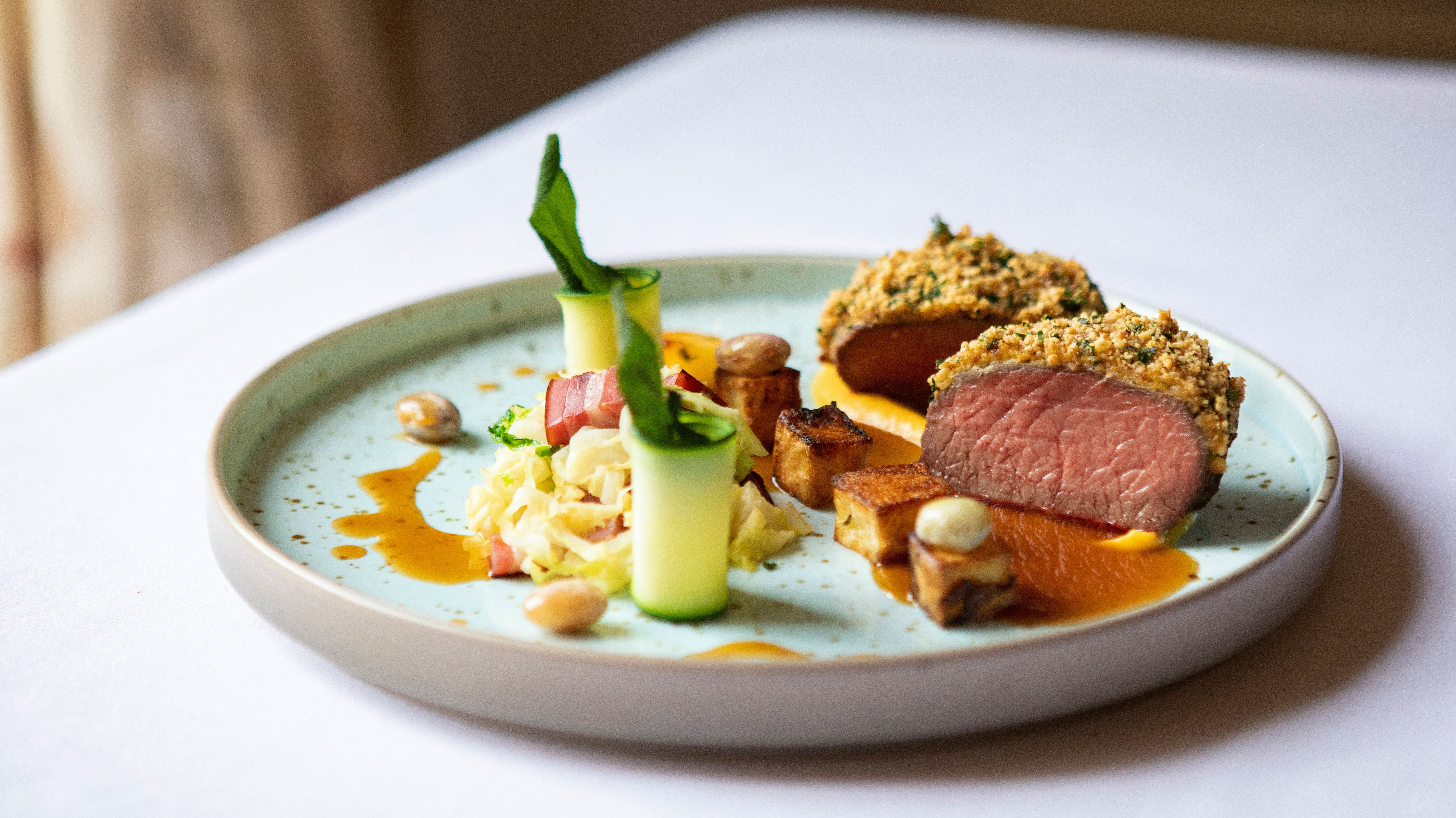Plated gourmet dish with sliced, herb-crusted meat, vegetables, and sauce