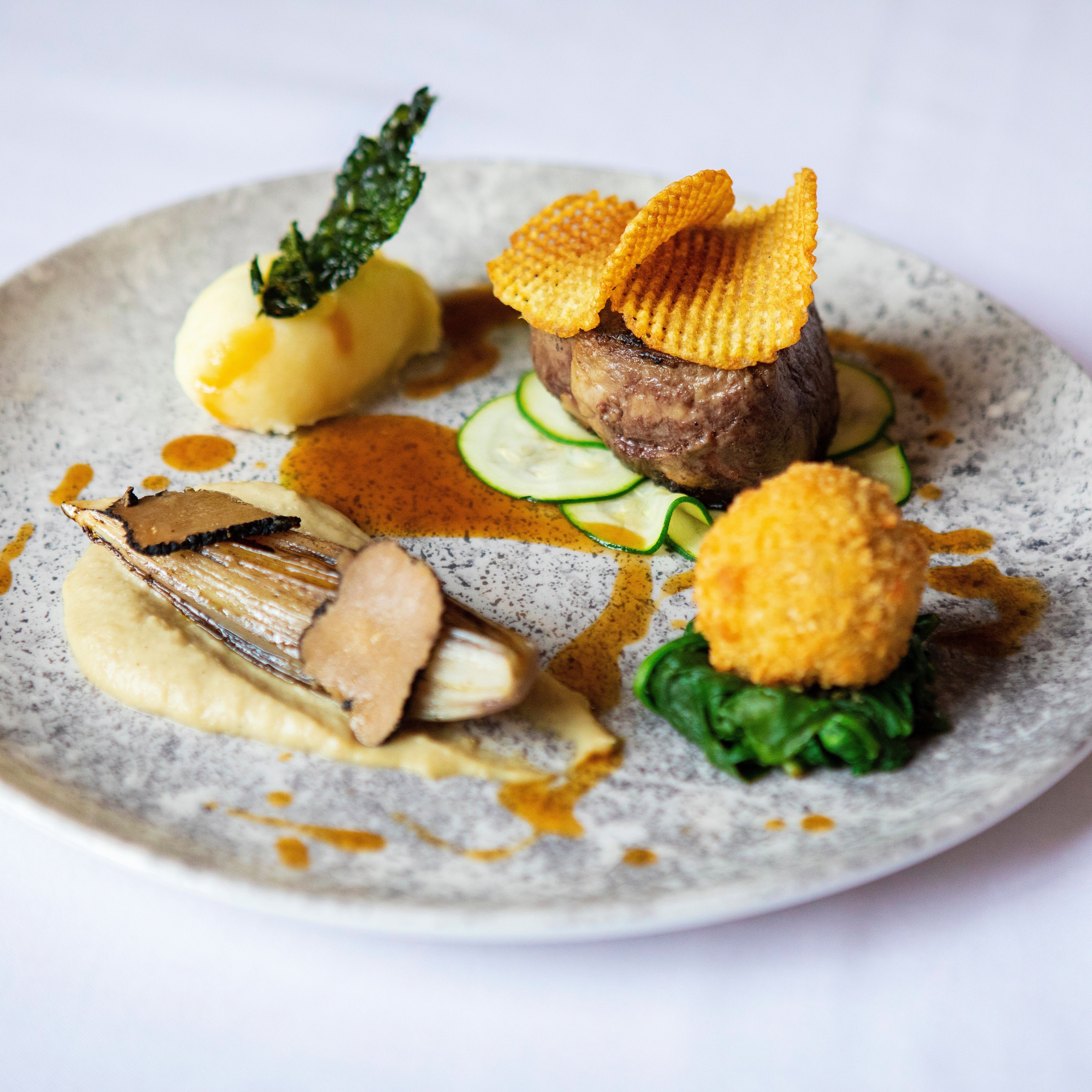 Gourmet plated dish with steak, potato, vegetables, and artistic garnishes