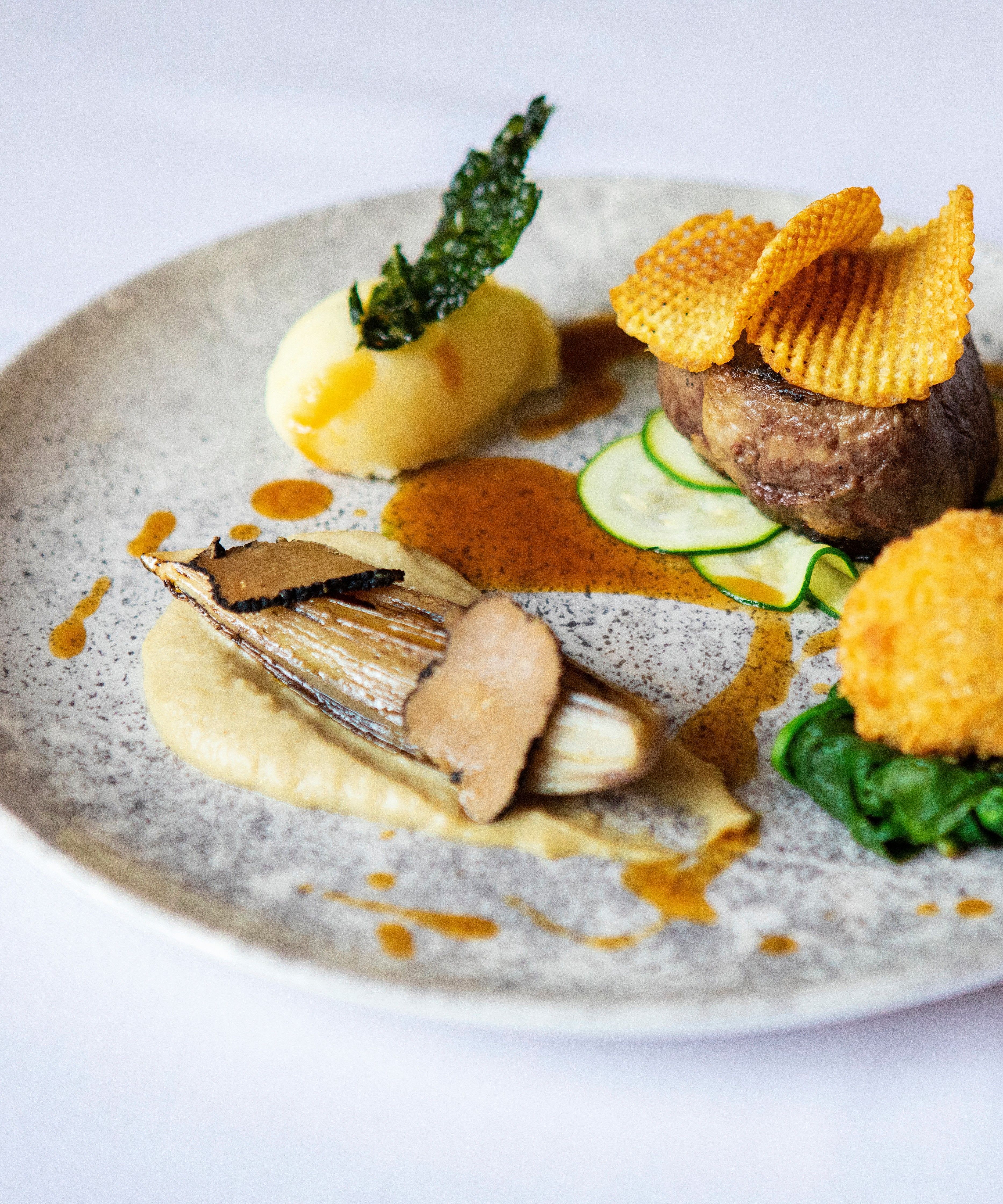 Gourmet plated dish with steak, potato, vegetables, and artistic garnishes