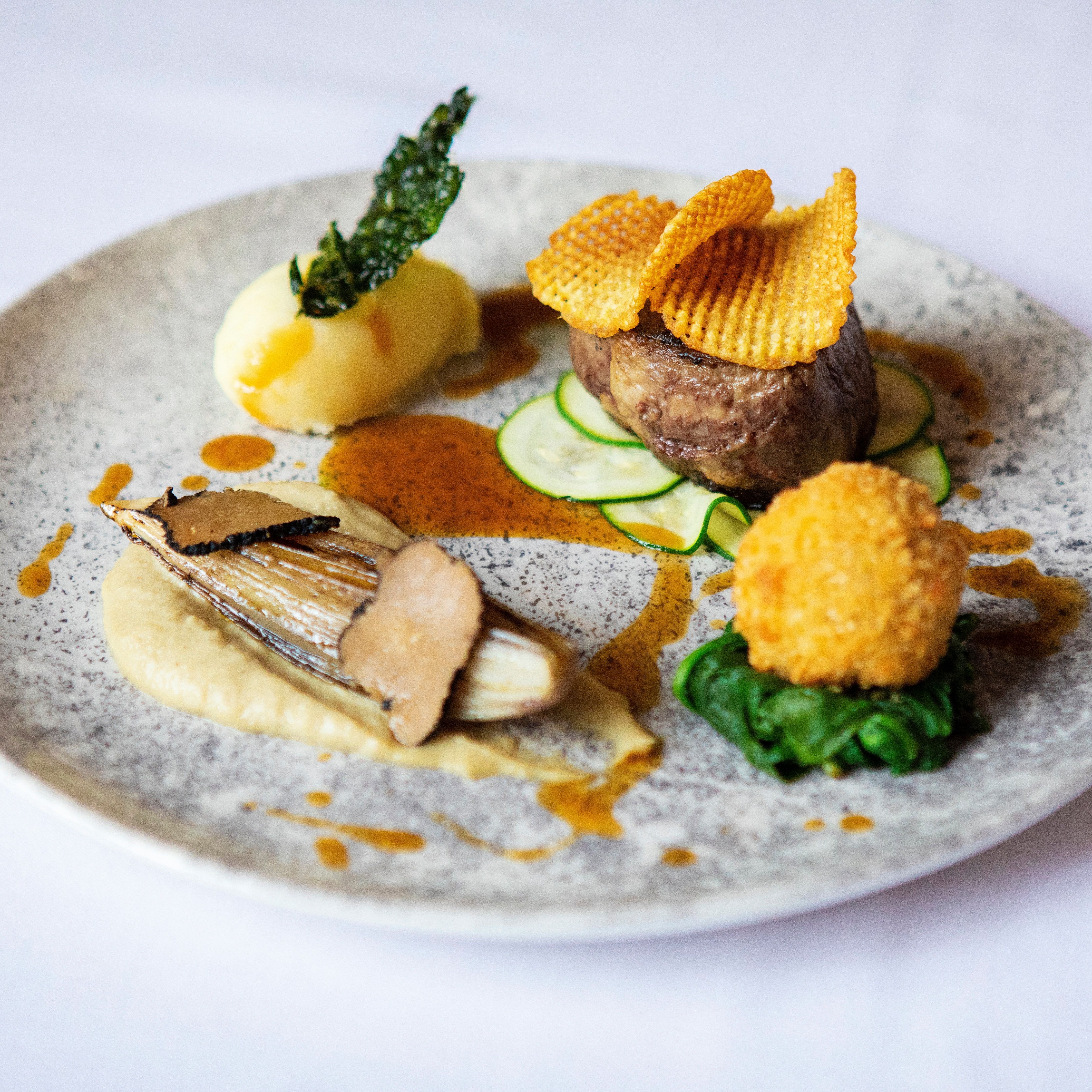 Gourmet plated dish with steak, potato, vegetables, and artistic garnishes
