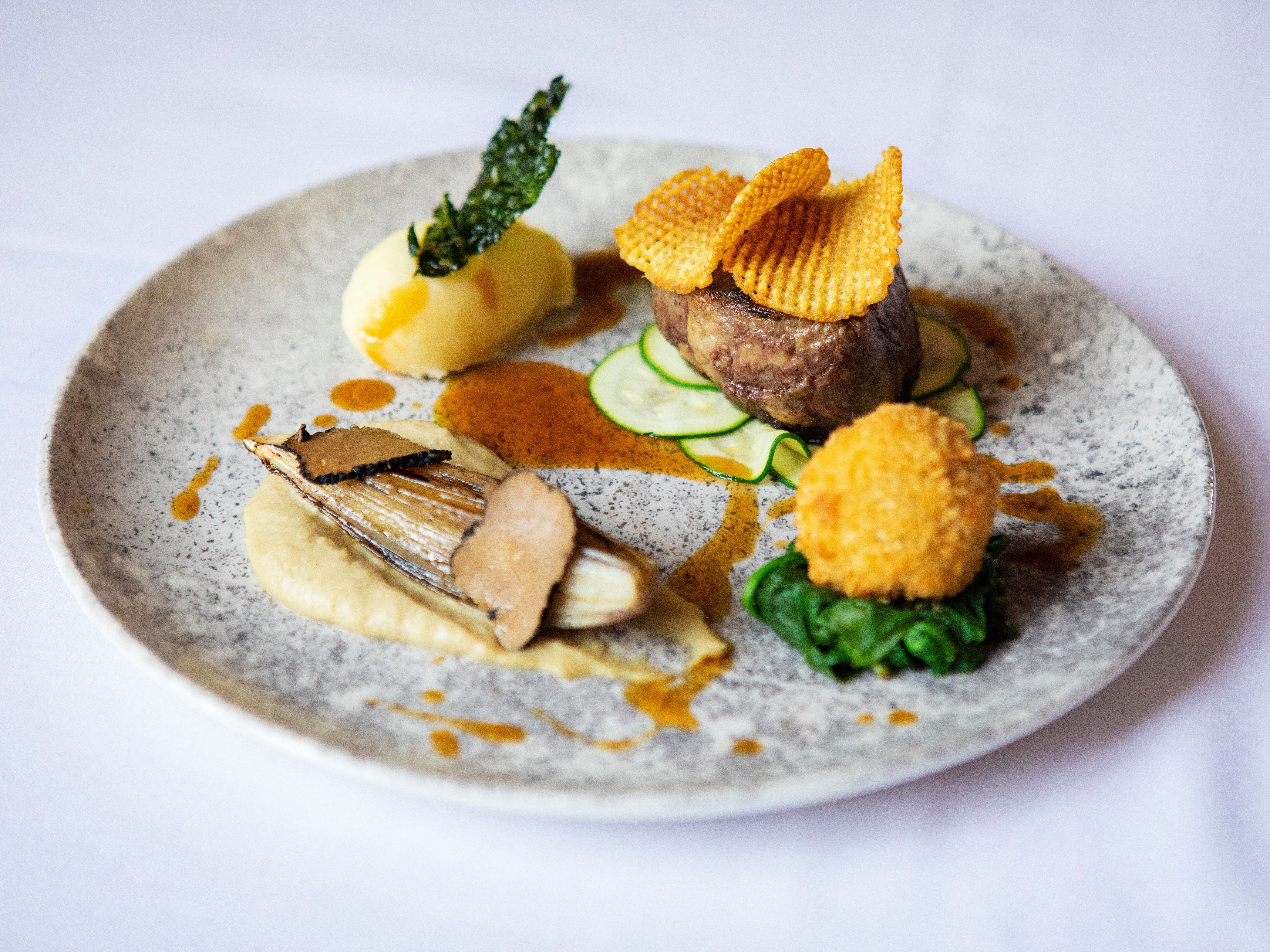 Gourmet plated dish with steak, potato, vegetables, and artistic garnishes