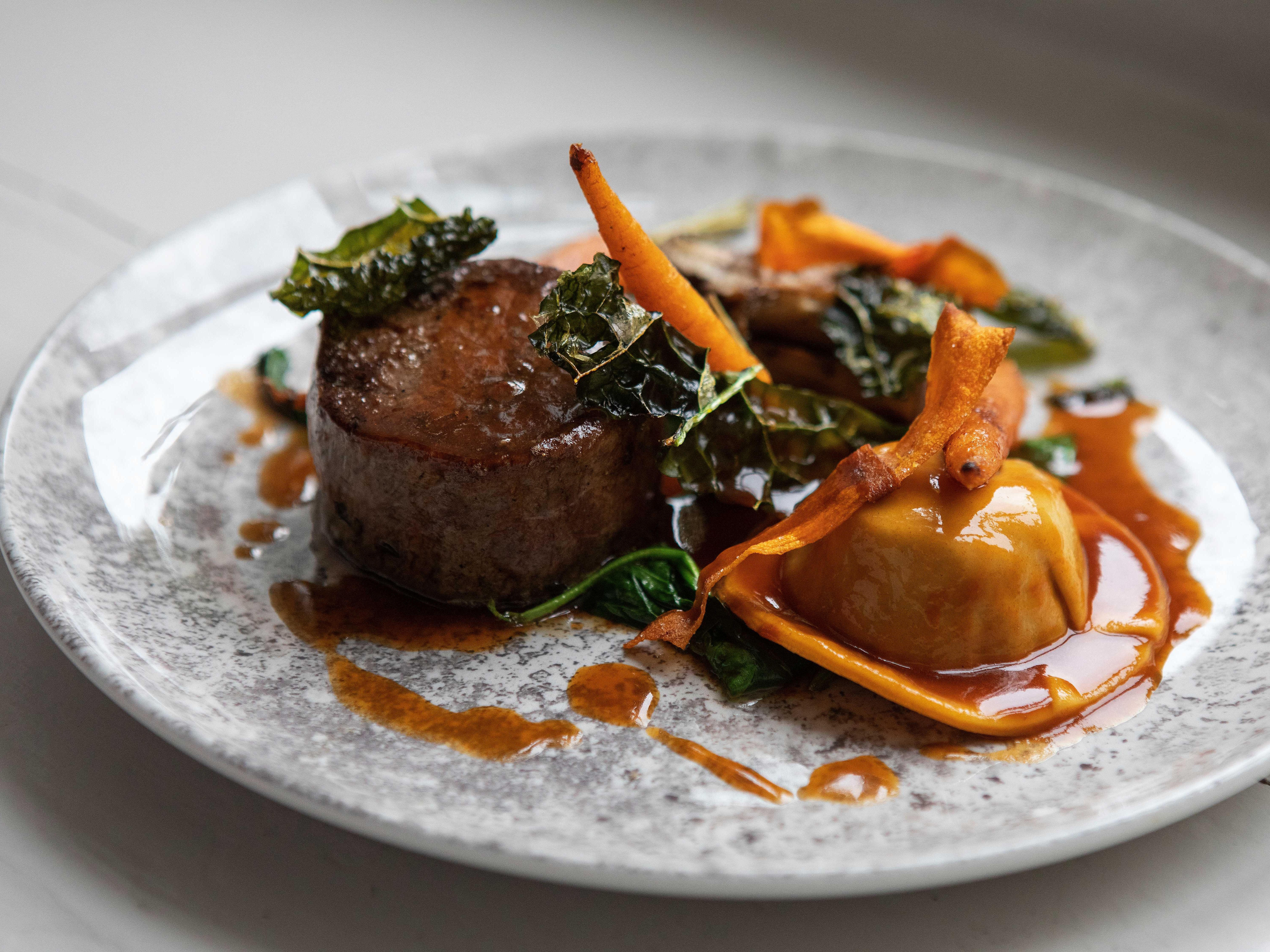 Gourmet plated dish with steak, ravioli, vegetables, and sauce