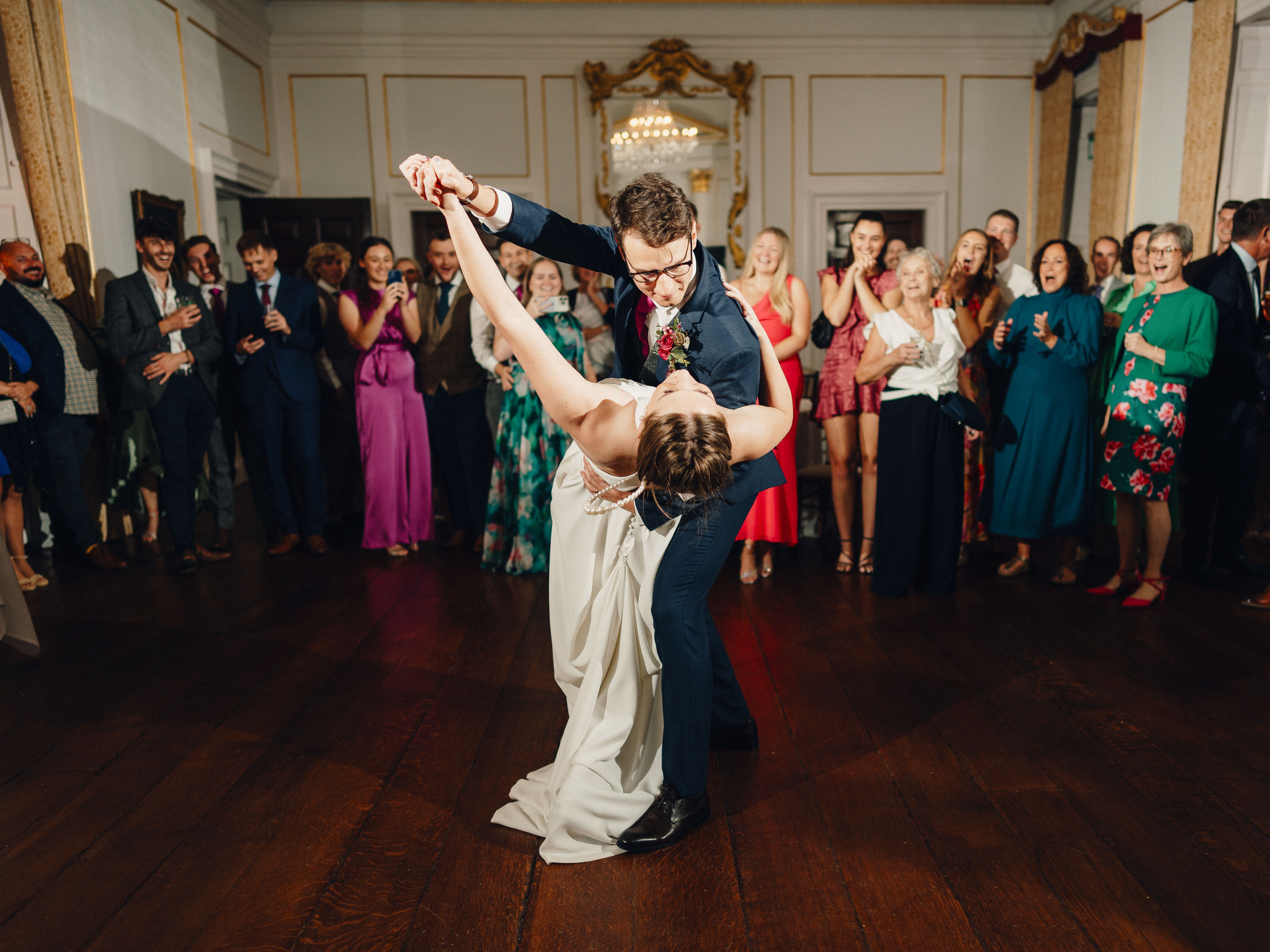 Bride and groom dancing in the center of a ballroom surrounded by wedding guests.
