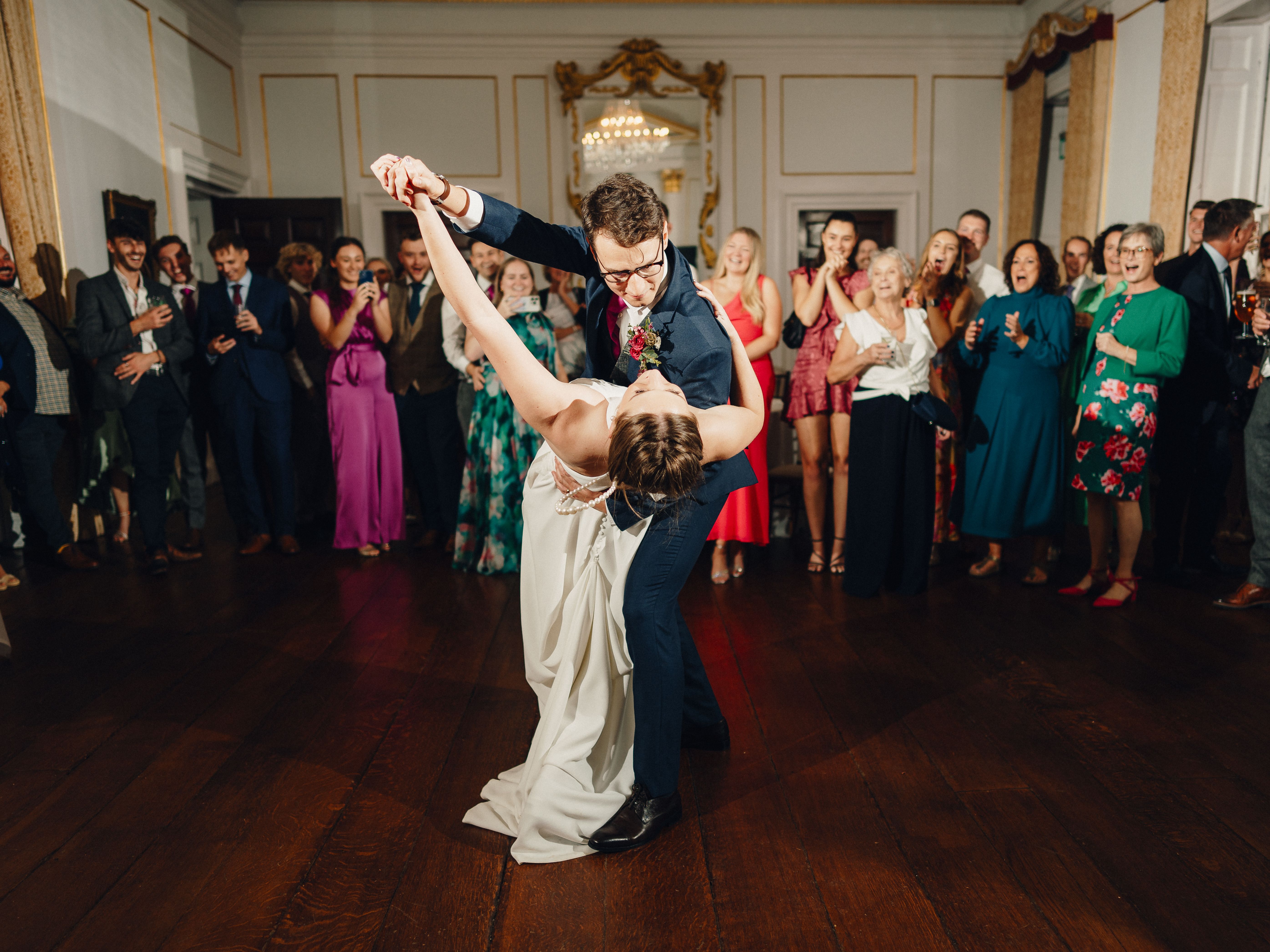 Bride and groom dancing in the center of a ballroom surrounded by wedding guests.