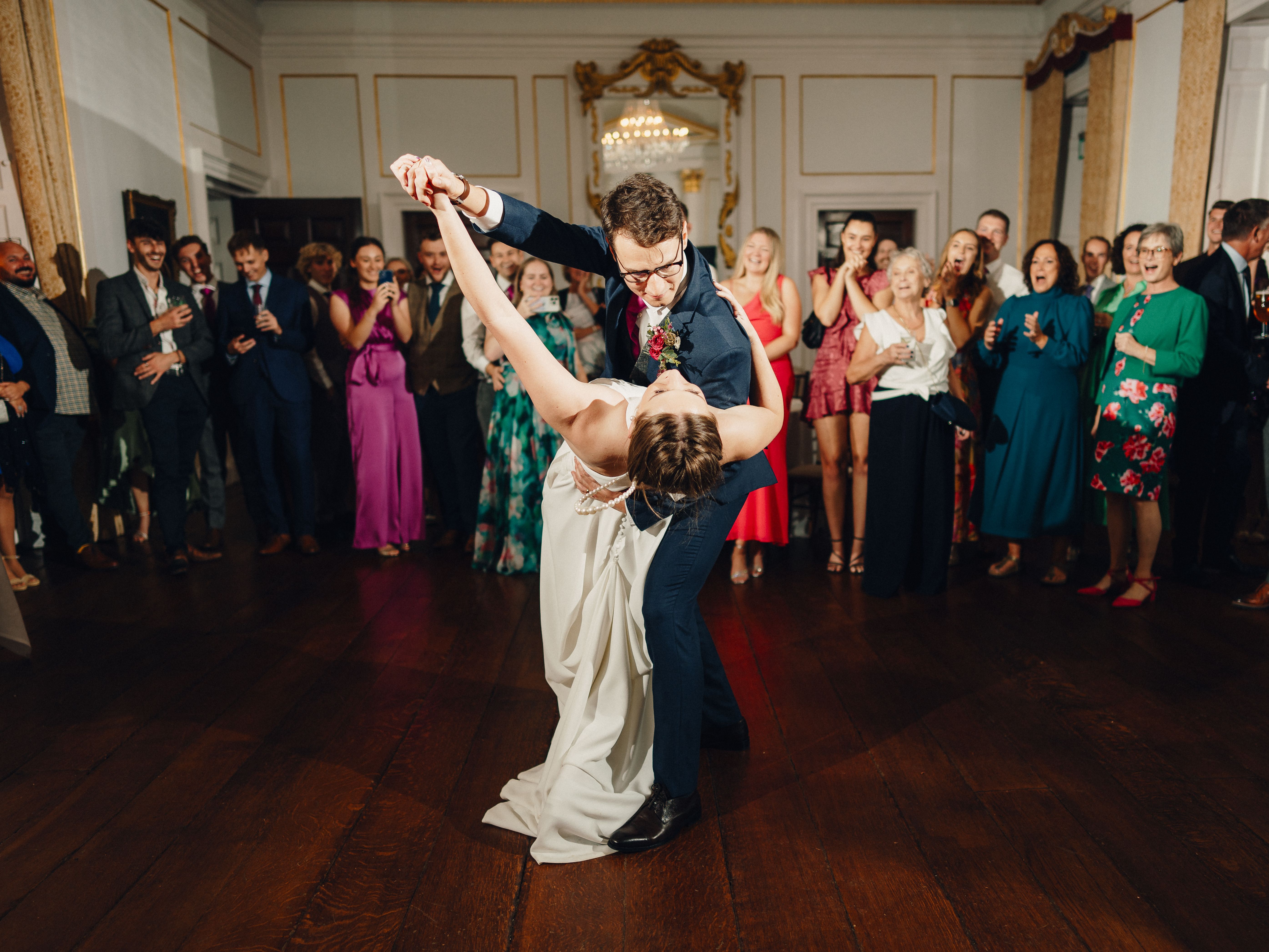 Bride and groom dancing in the center of a ballroom surrounded by wedding guests.