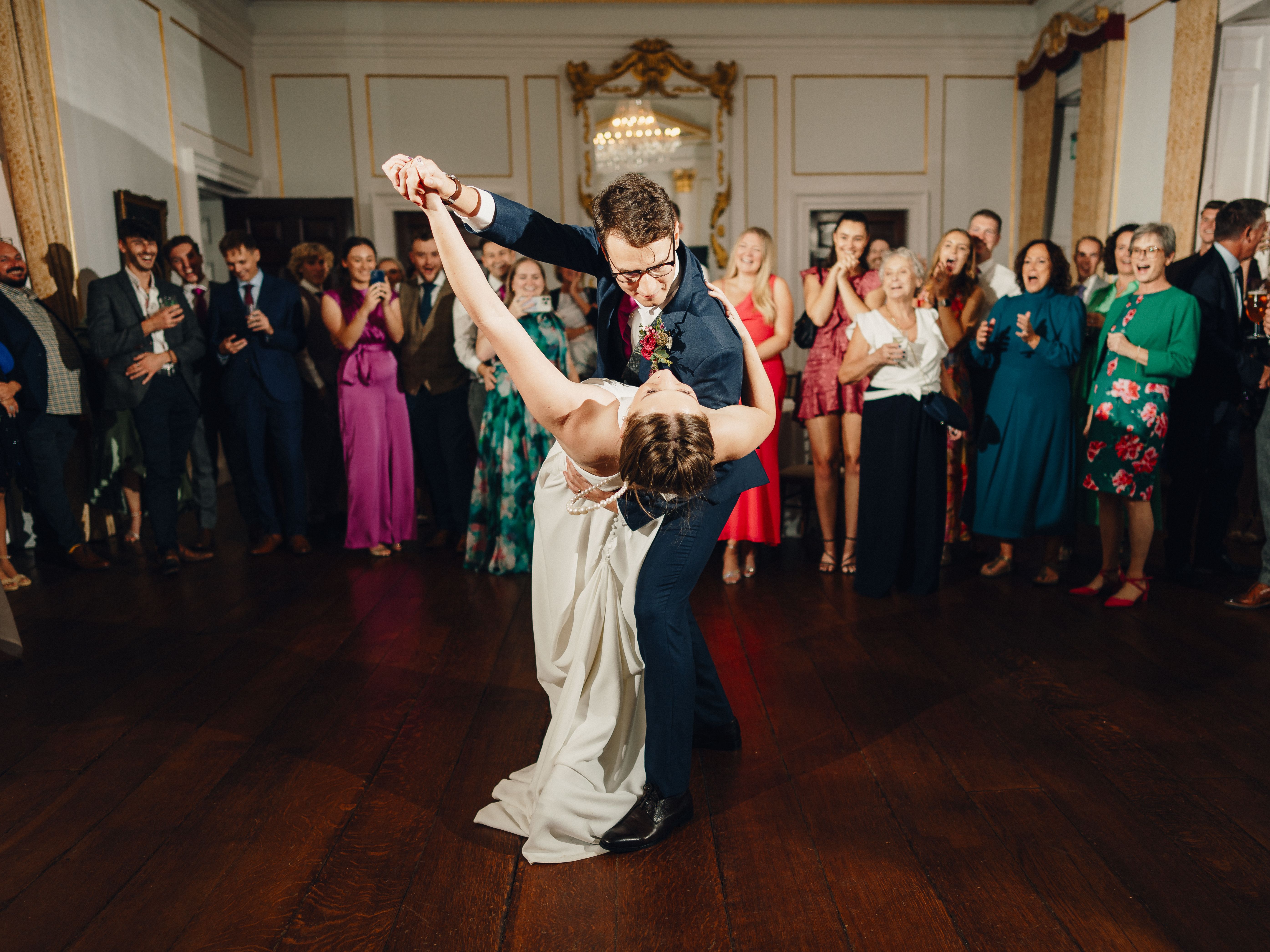 Bride and groom dancing in the center of a ballroom surrounded by wedding guests.