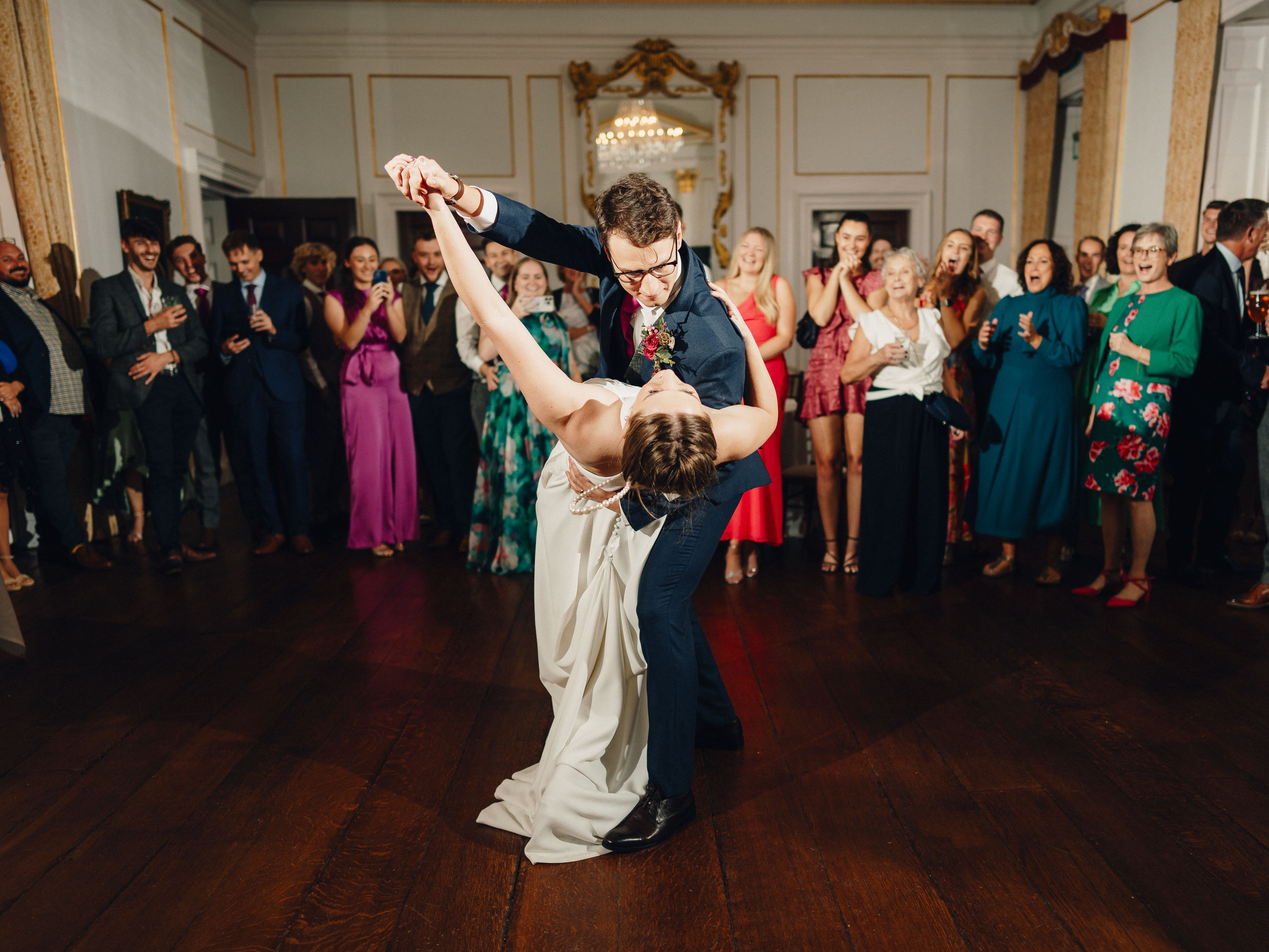 Bride and groom dancing in the center of a ballroom surrounded by wedding guests.