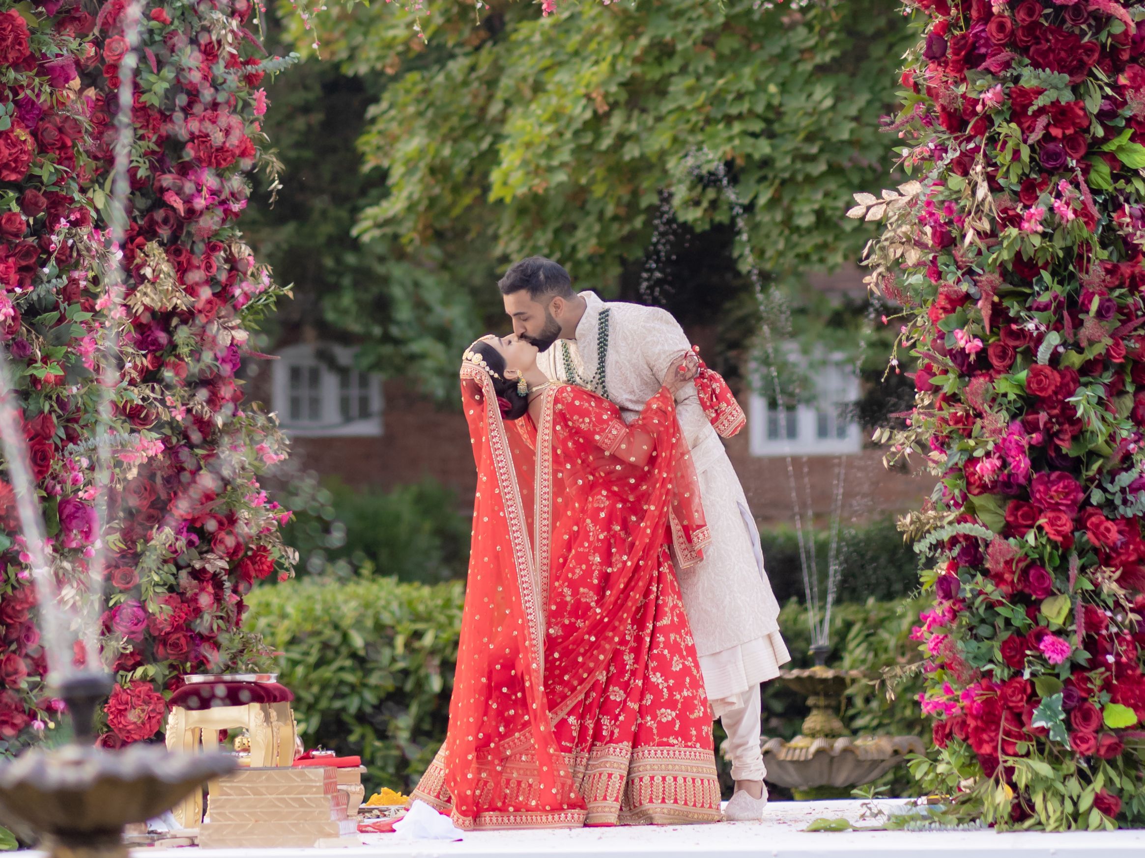 Indian wedding couple kissing under a floral arch outdoors