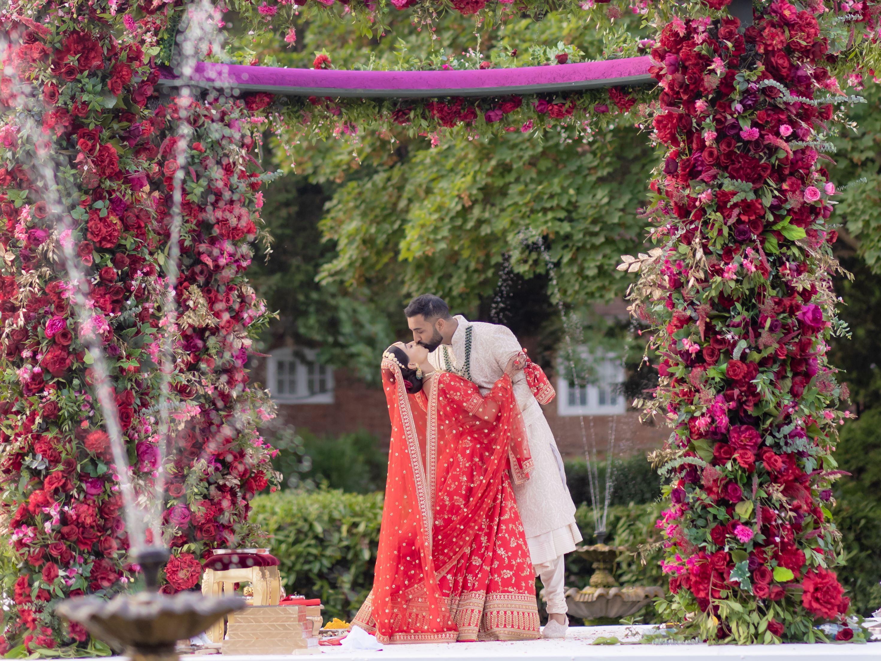 Indian wedding couple kissing under a floral arch outdoors