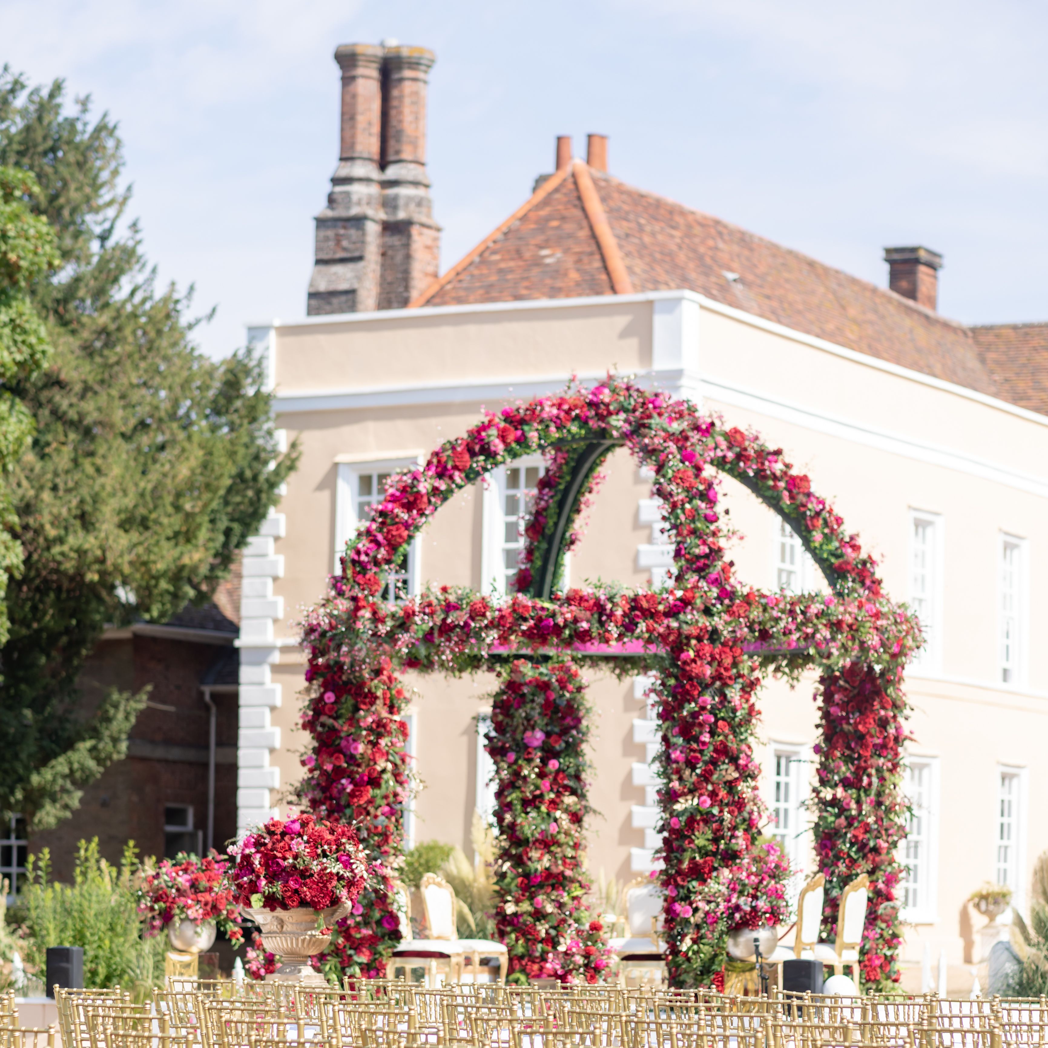 Outdoor wedding ceremony setup with golden chairs and a floral arch in front of an elegant mansion.