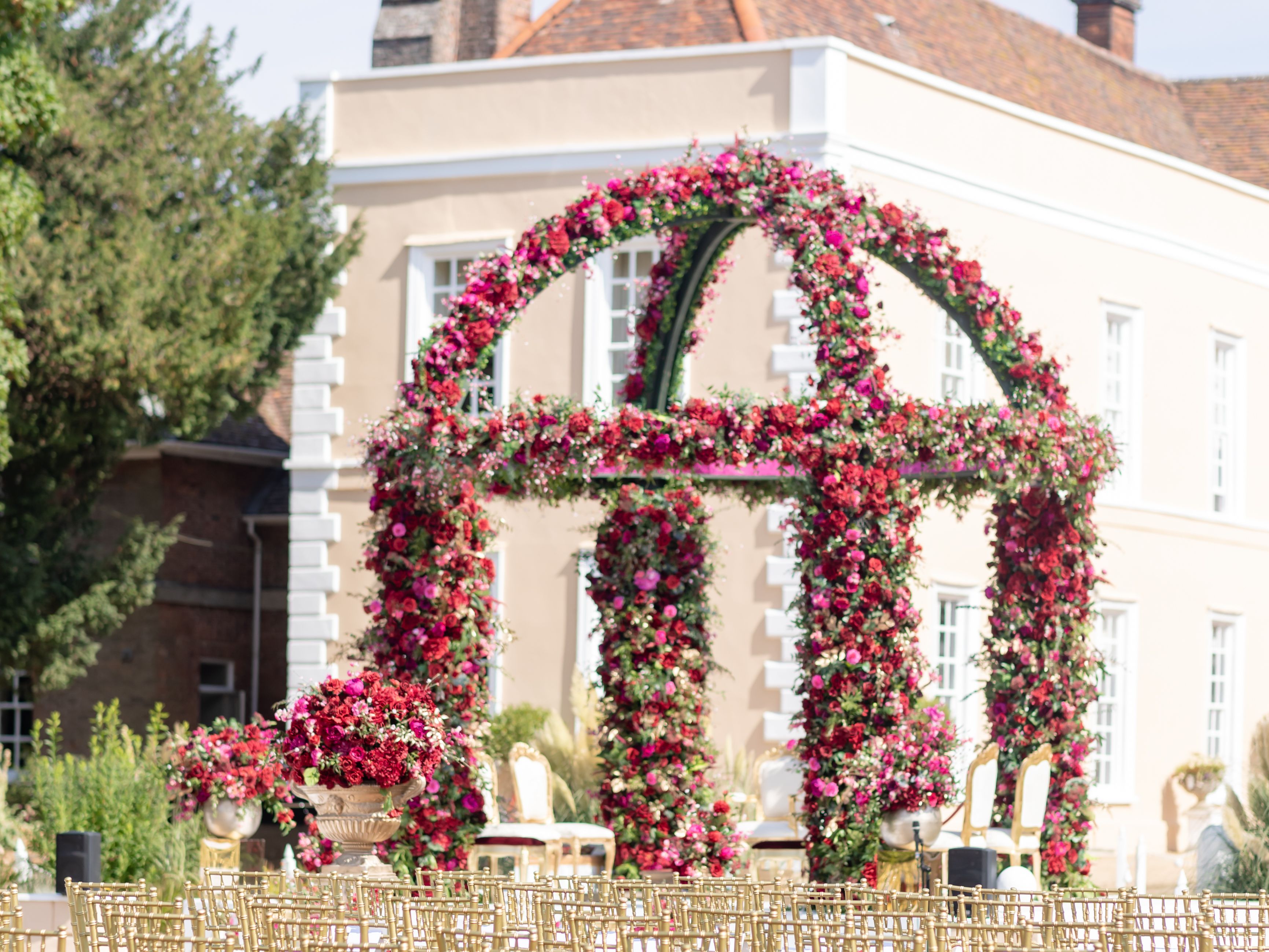 Outdoor wedding ceremony setup with golden chairs and a floral arch in front of an elegant mansion.