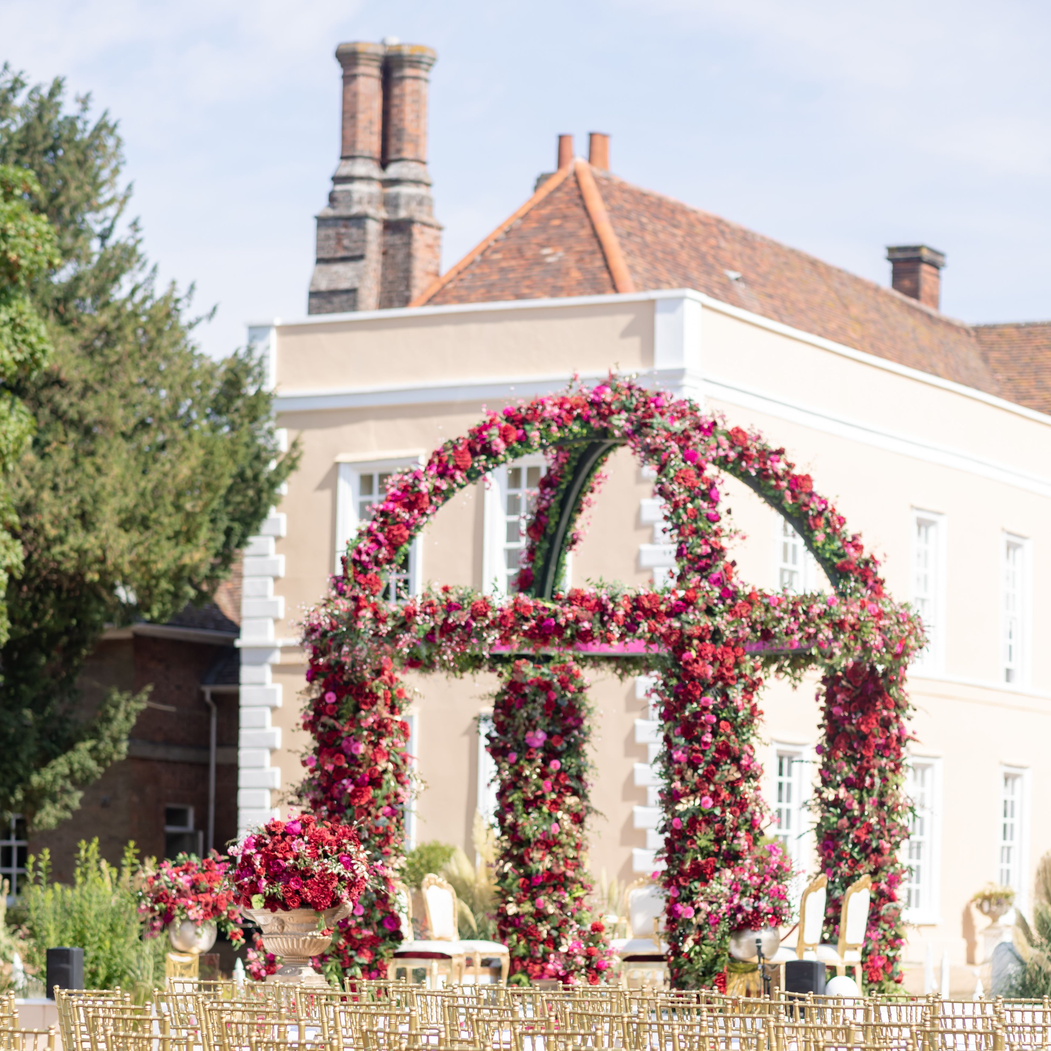 Outdoor wedding ceremony setup with golden chairs and a floral arch in front of an elegant mansion.
