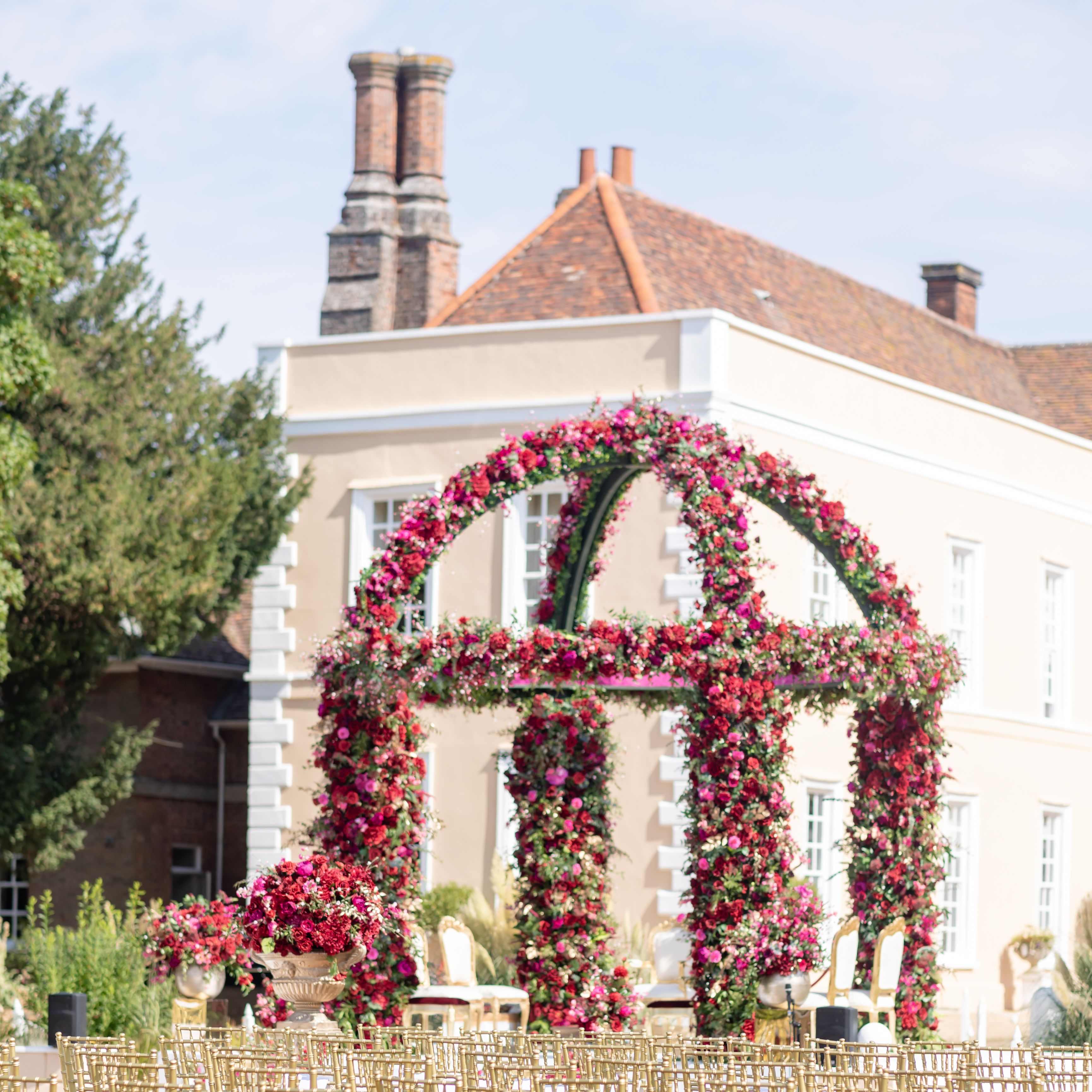 Outdoor wedding ceremony setup with golden chairs and a floral arch in front of an elegant mansion.
