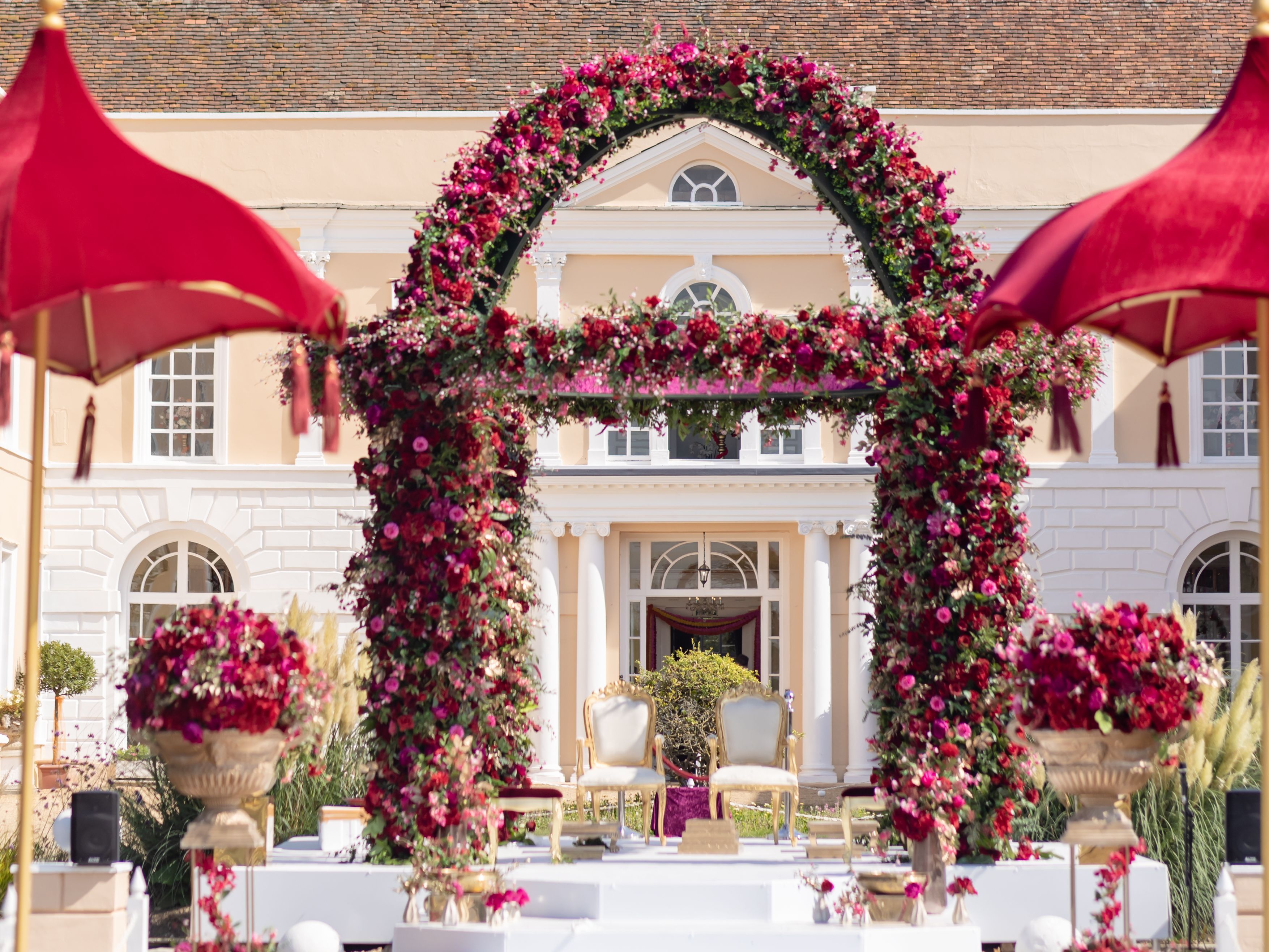 Outdoor wedding mandap decorated with pink and red flowers in front of a large mansion