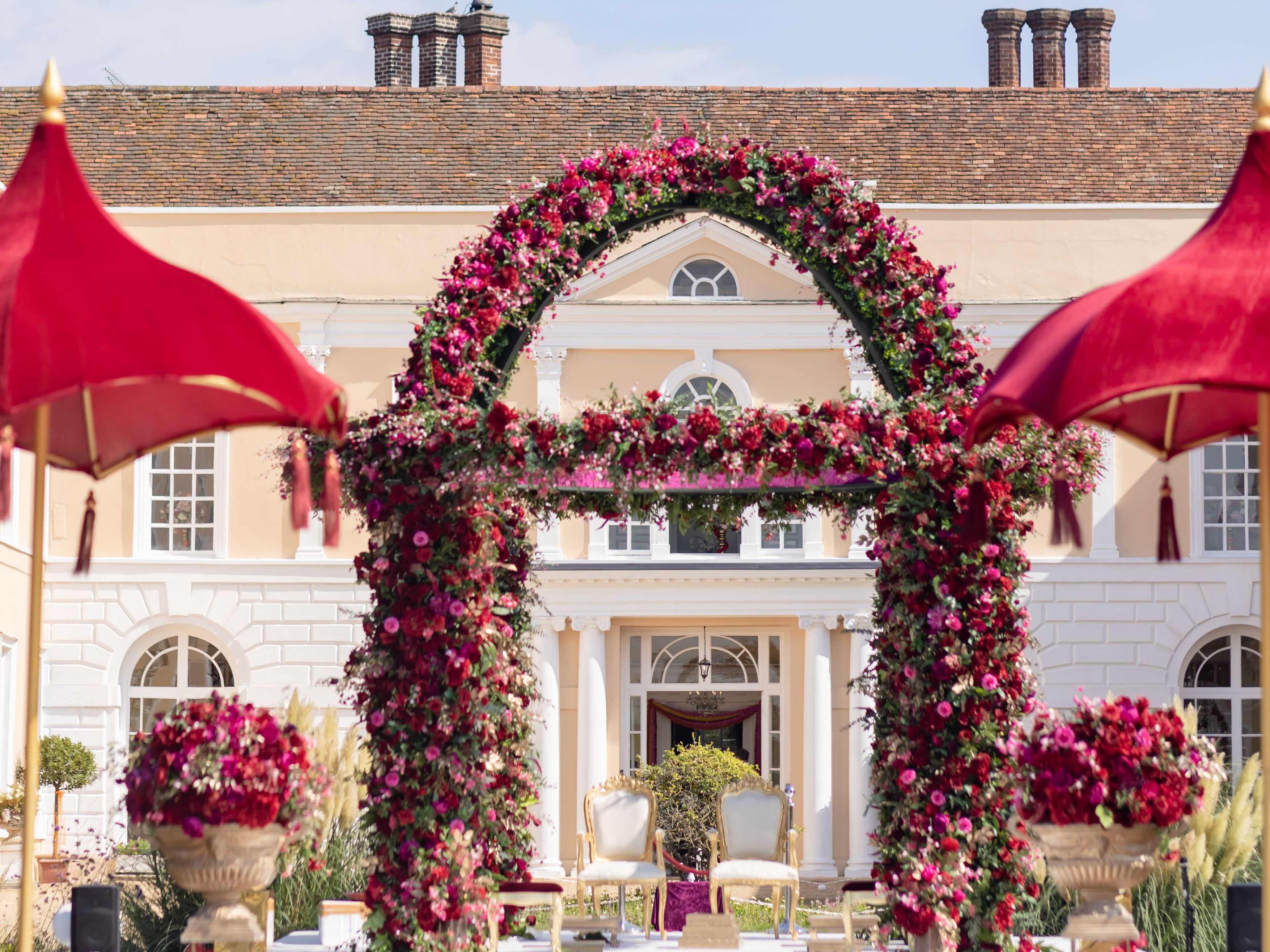 Outdoor wedding mandap decorated with pink and red flowers in front of a large mansion