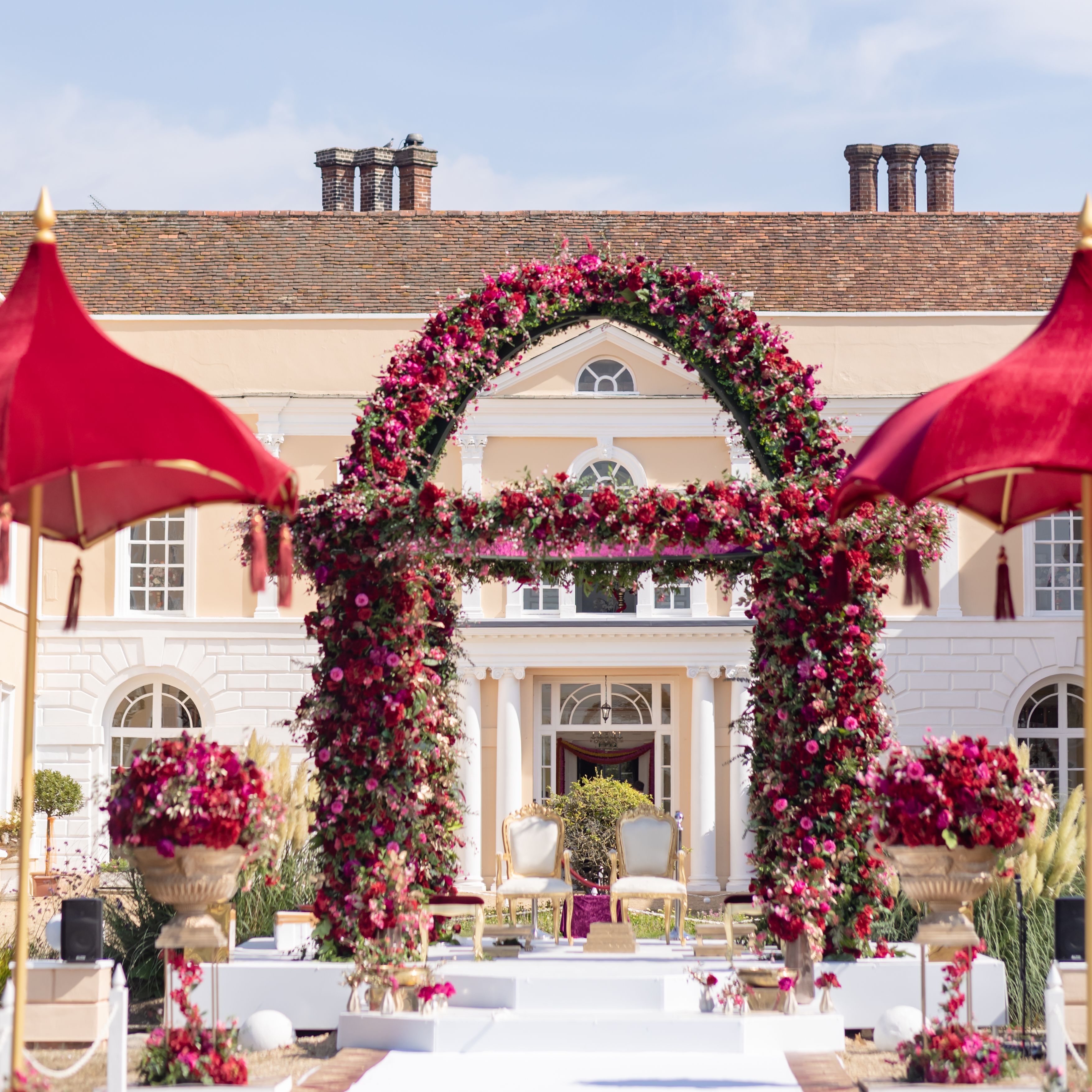 Outdoor wedding mandap decorated with pink and red flowers in front of a large mansion