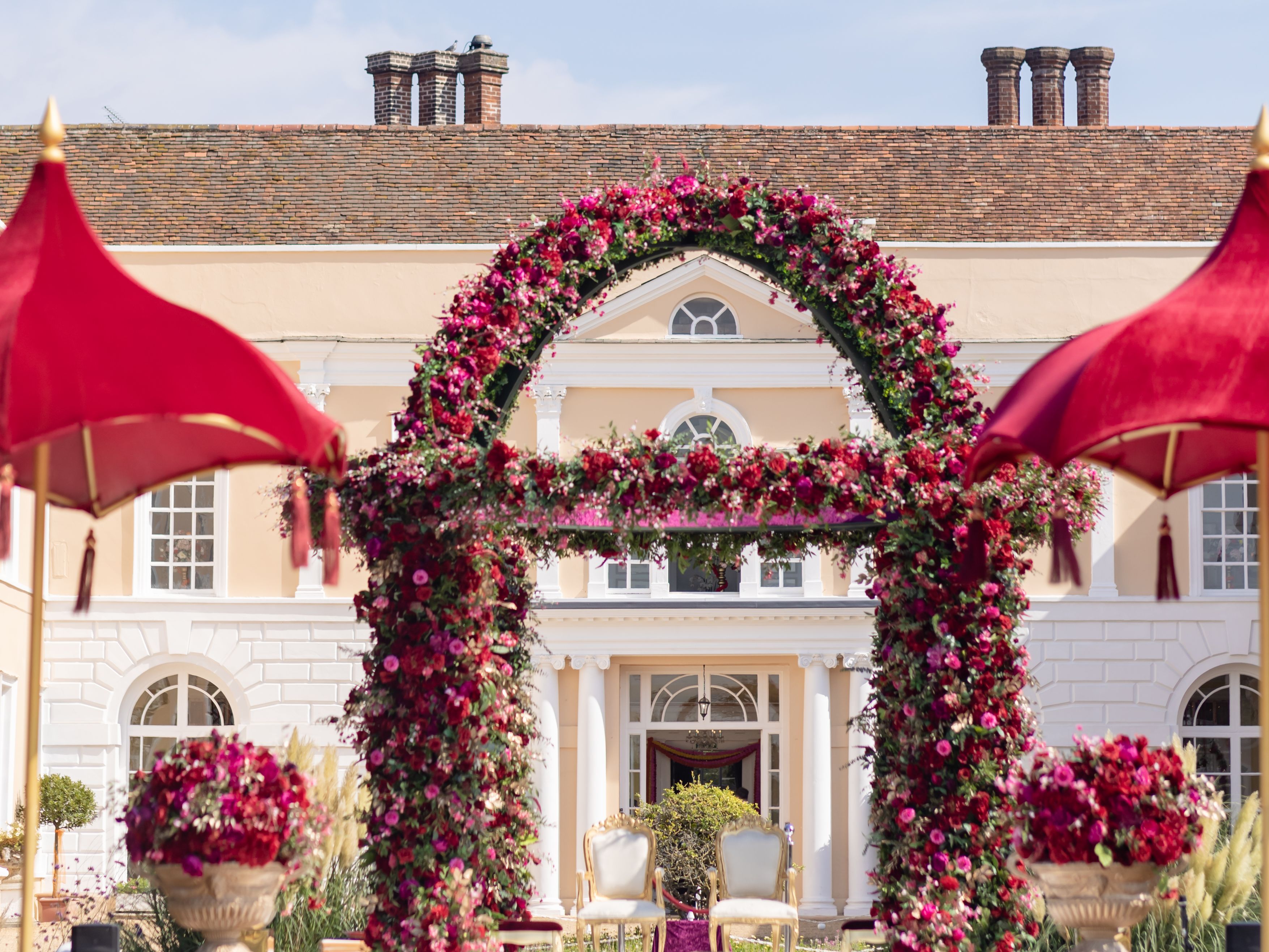 Outdoor wedding mandap decorated with pink and red flowers in front of a large mansion